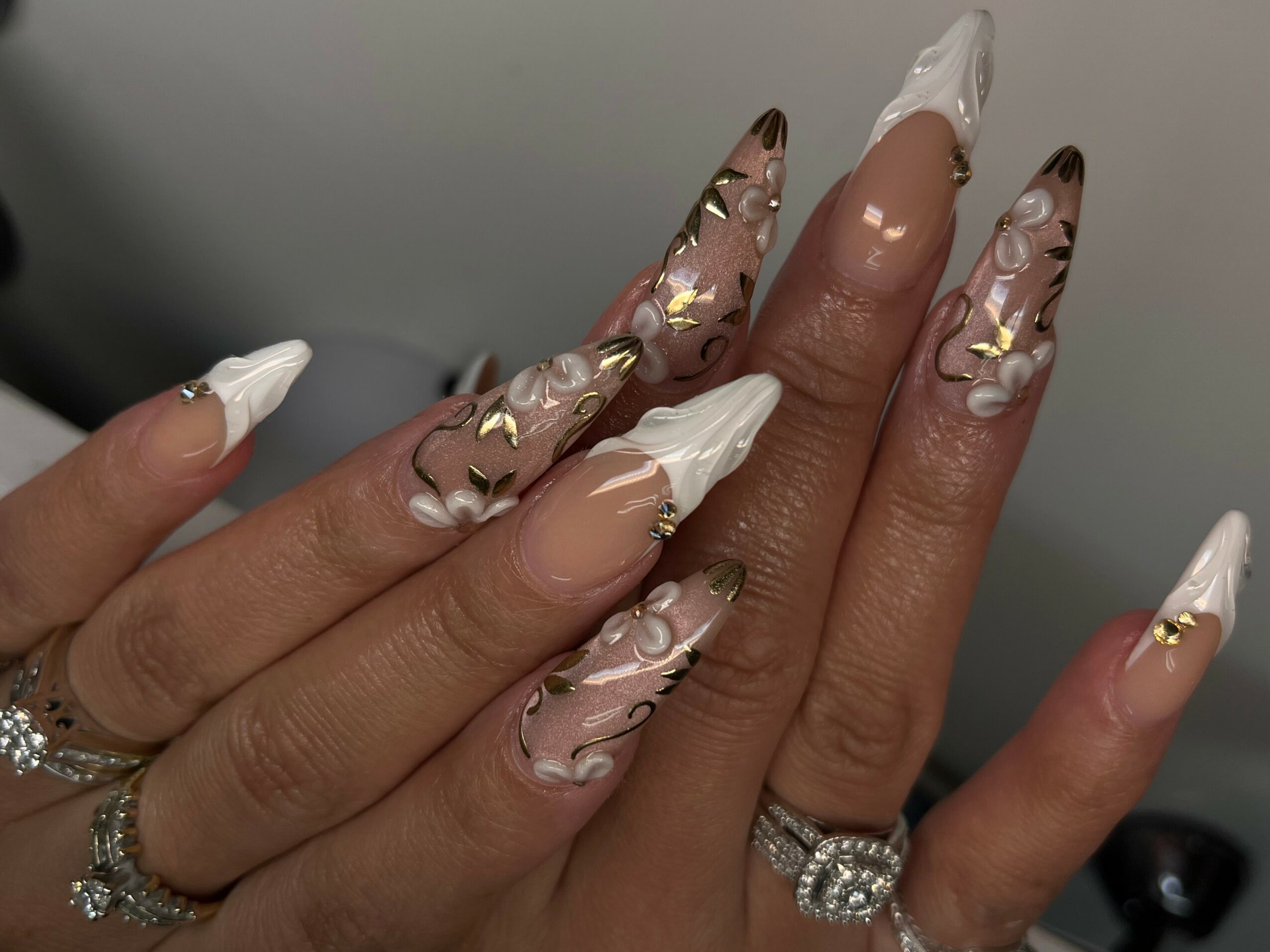 Close-up of long, decorated nails with white, pink, and gold accents, and rings on fingers.