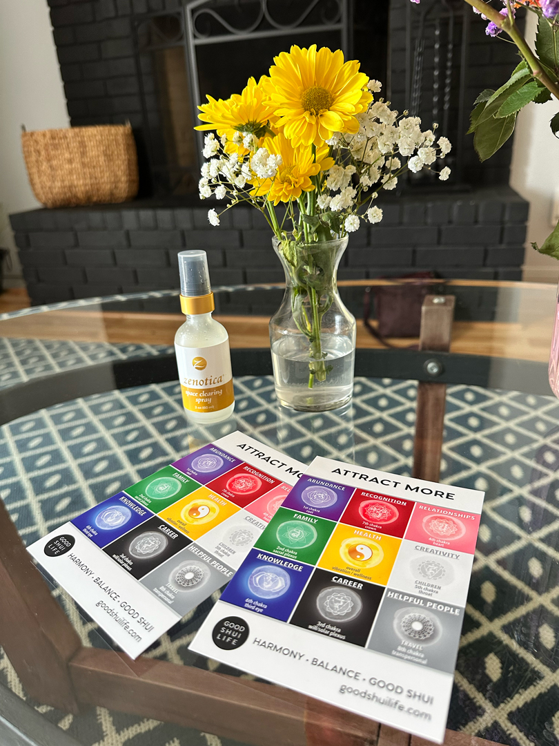 Vase with yellow and white flowers on table, attract mode card, spray bottle, and black object, patterned tablecloth.
