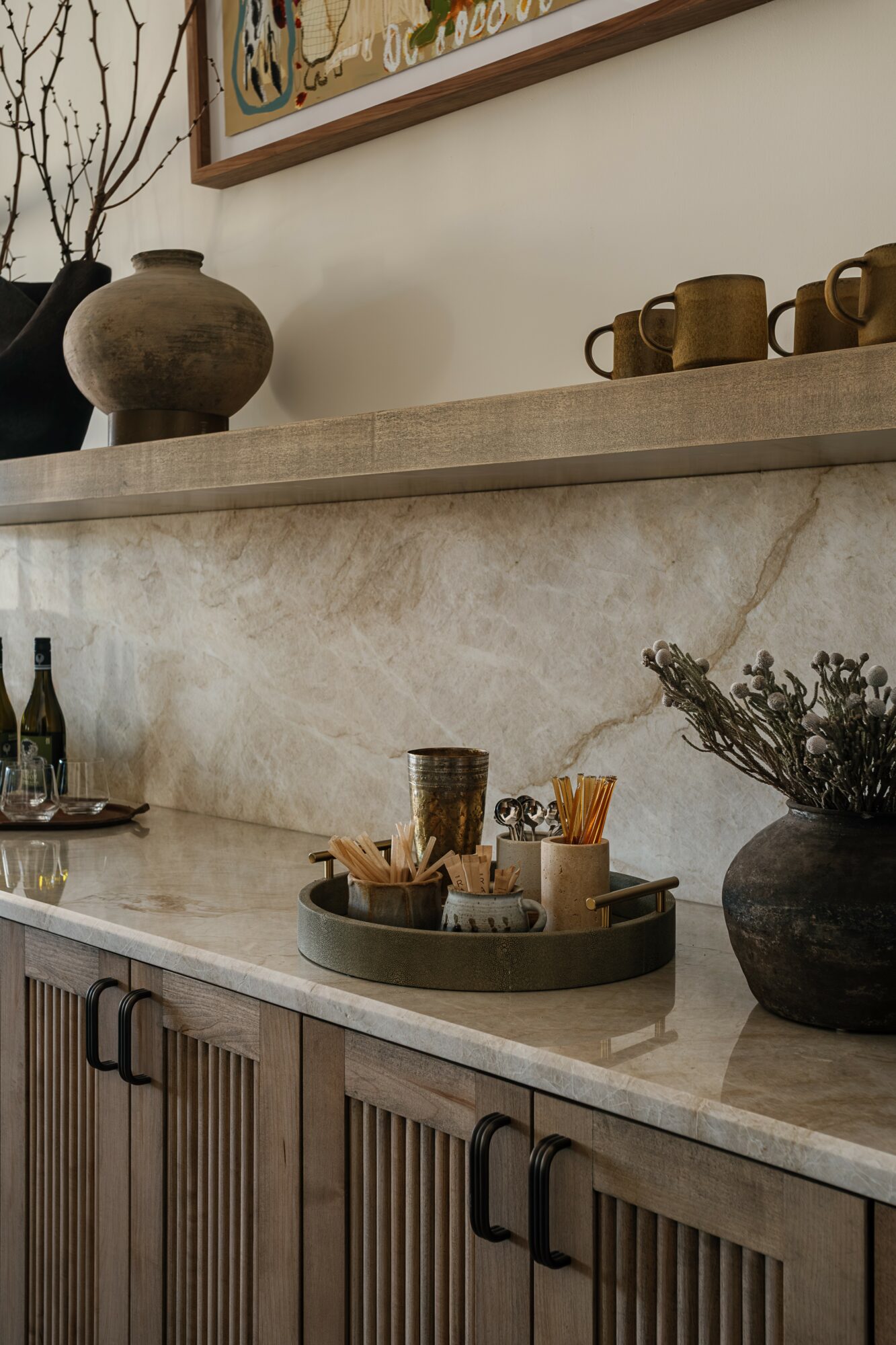 Kitchen counter with decorative vases, cups, and a tray with utensils, against a wall with a framed picture.