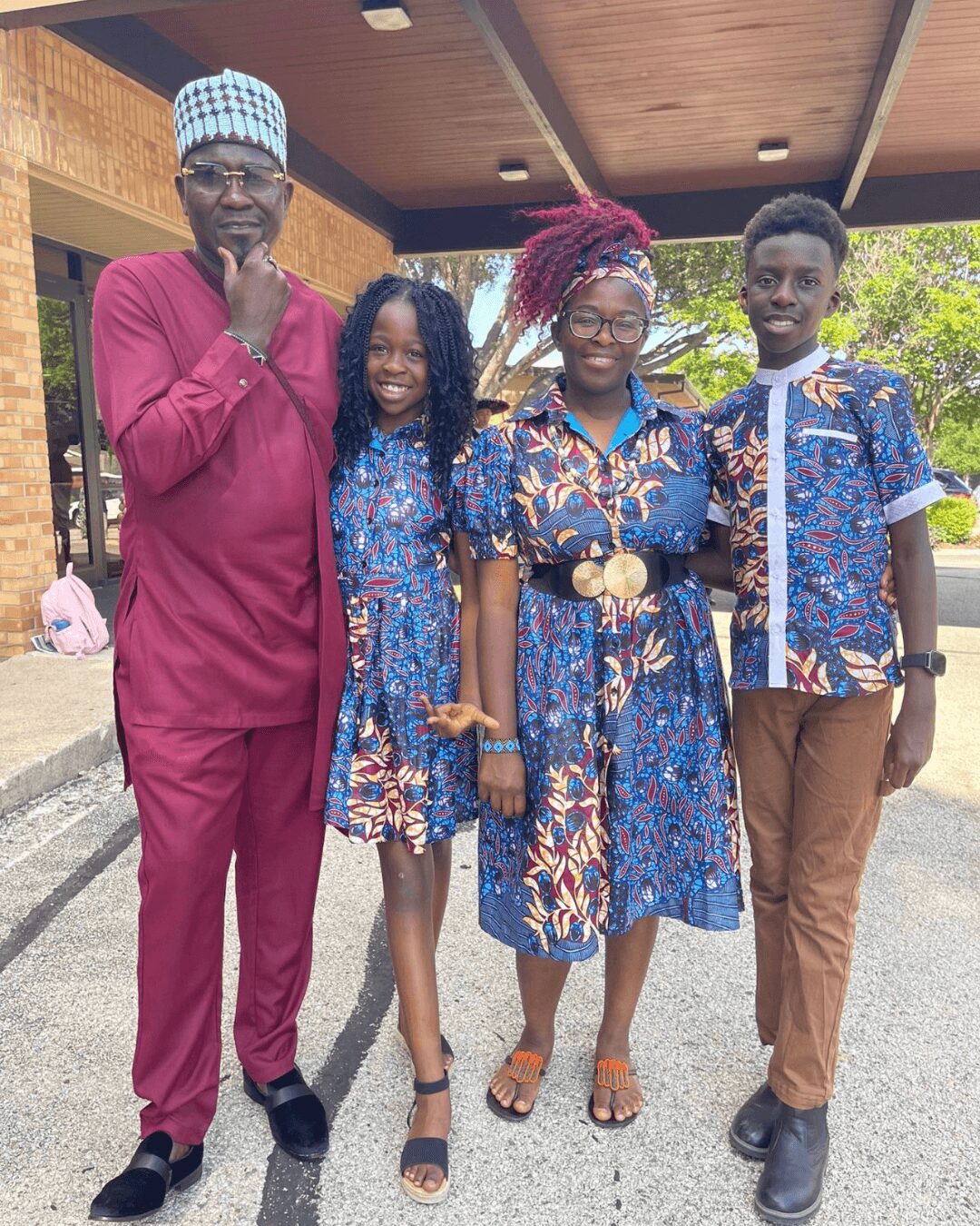 Four people standing outdoors, smiling, with trees and a building in the background.