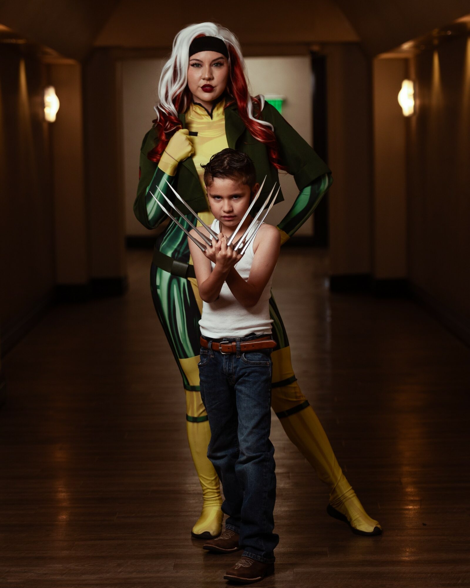 Woman in colorful costume standing behind a young boy in a hallway with warm lighting.