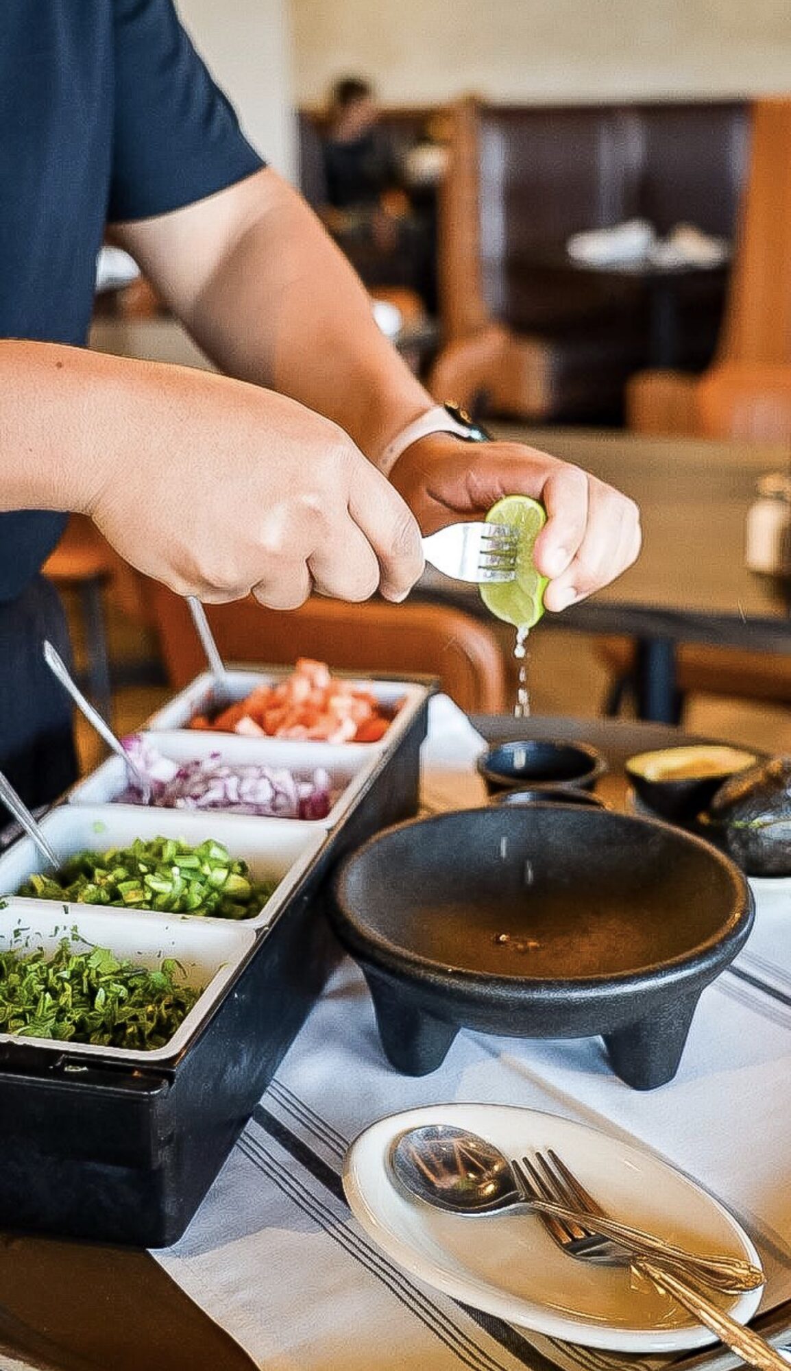 Person pouring green sauce from a squeeze bottle onto food in a restaurant setting.