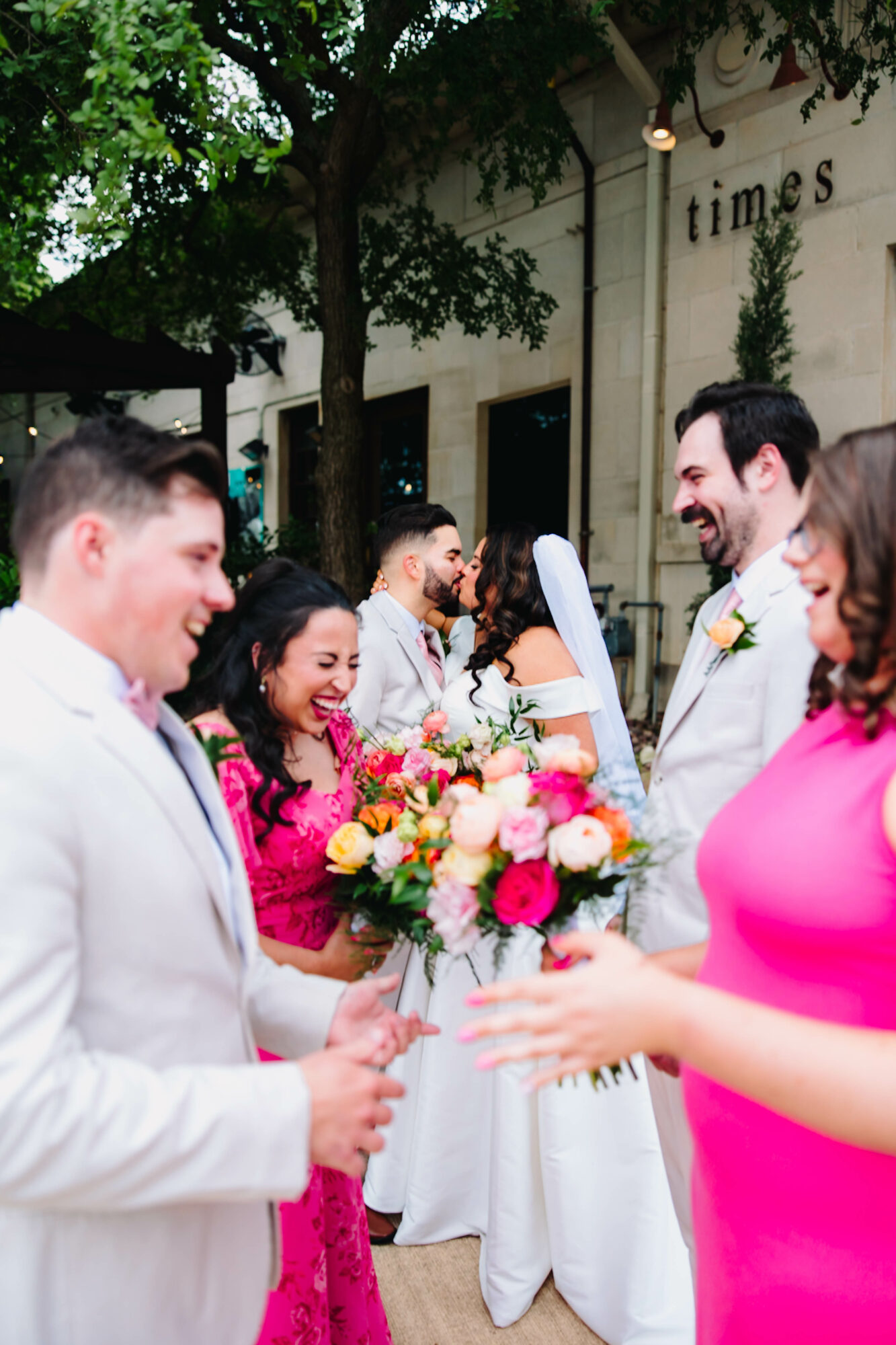 Group of people smiling and exchanging flowers outdoors, with a building and trees in the background.