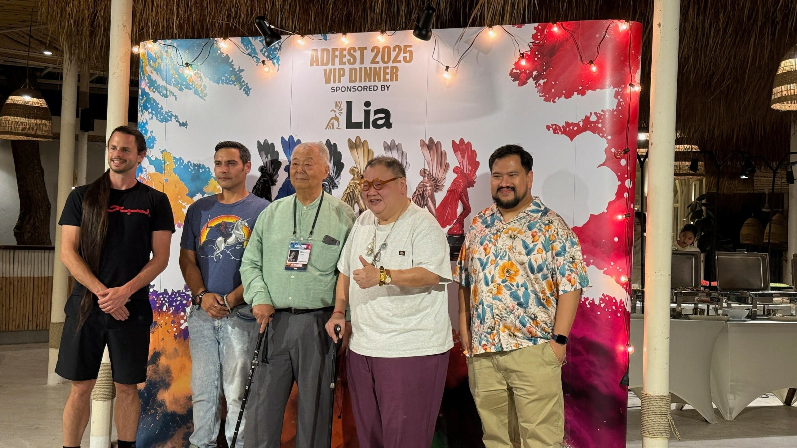 Five people standing in front of a colorful event backdrop, smiling and posing for the photo.