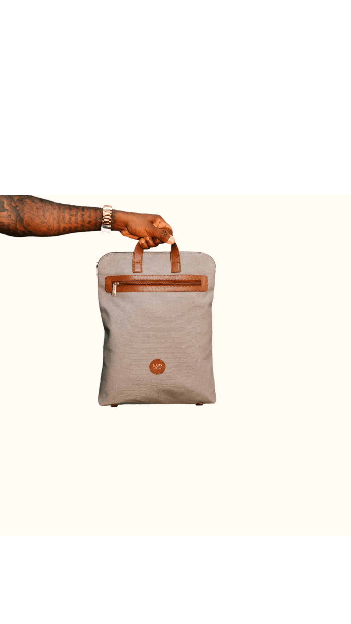 Hand holding a beige bag with a handle and a small circular logo, against a white background.