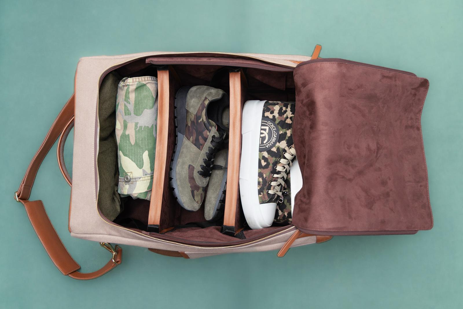 Open bag with four pairs of shoes inside, divided by compartments, on a teal surface.