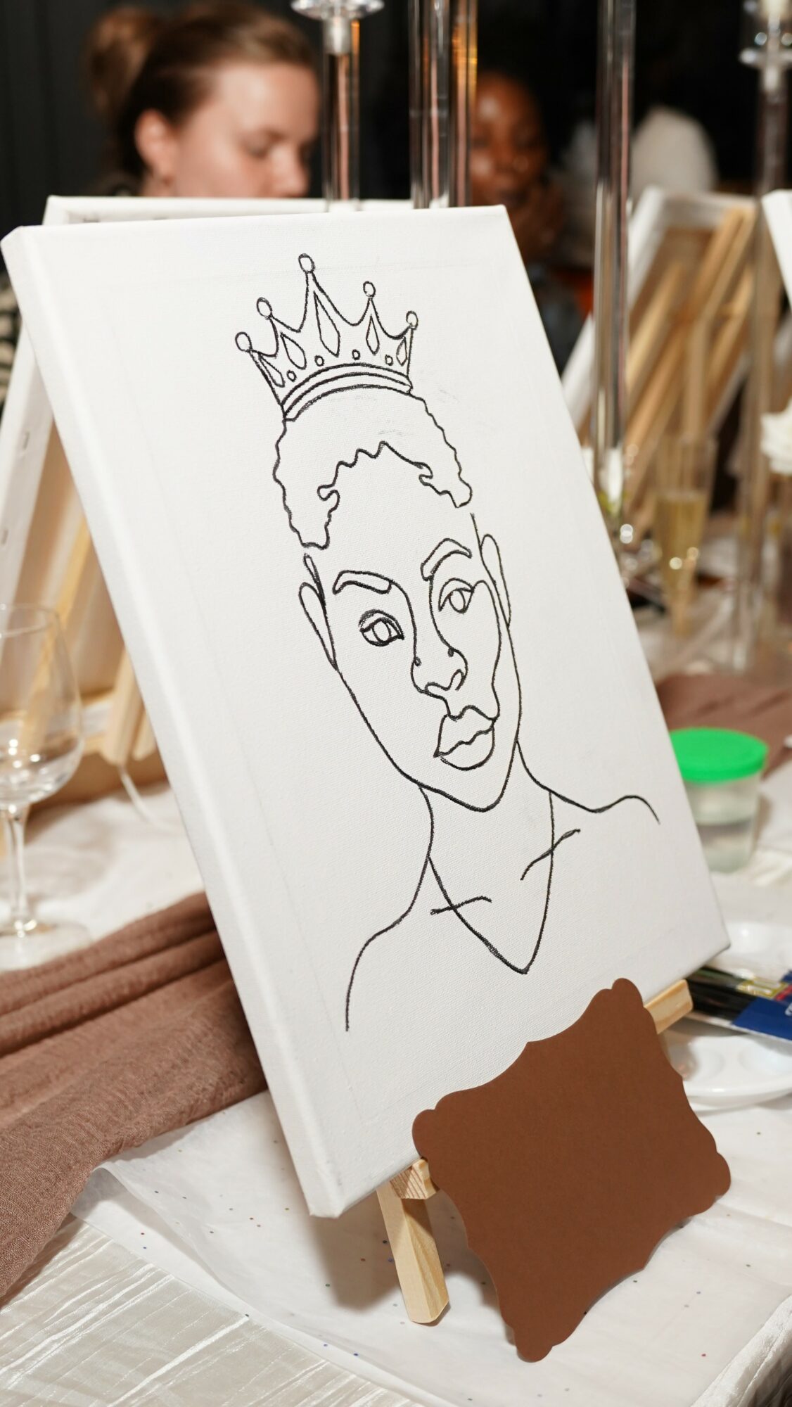 Line drawing of a woman with a crown on her head, on a white canvas, in a busy setting.