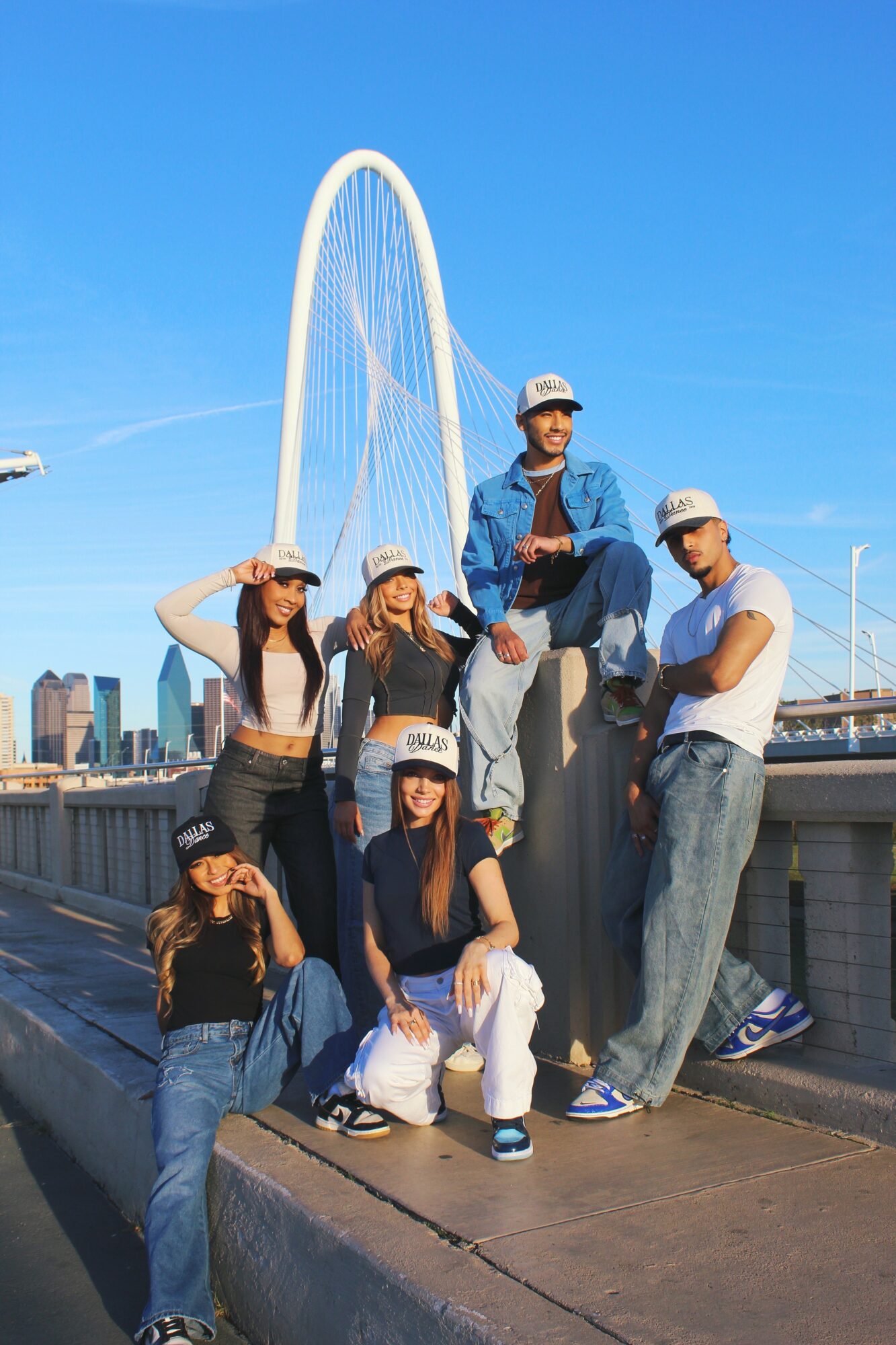 Group of six people posing on a rooftop with a city skyline and a large arch bridge in the background.