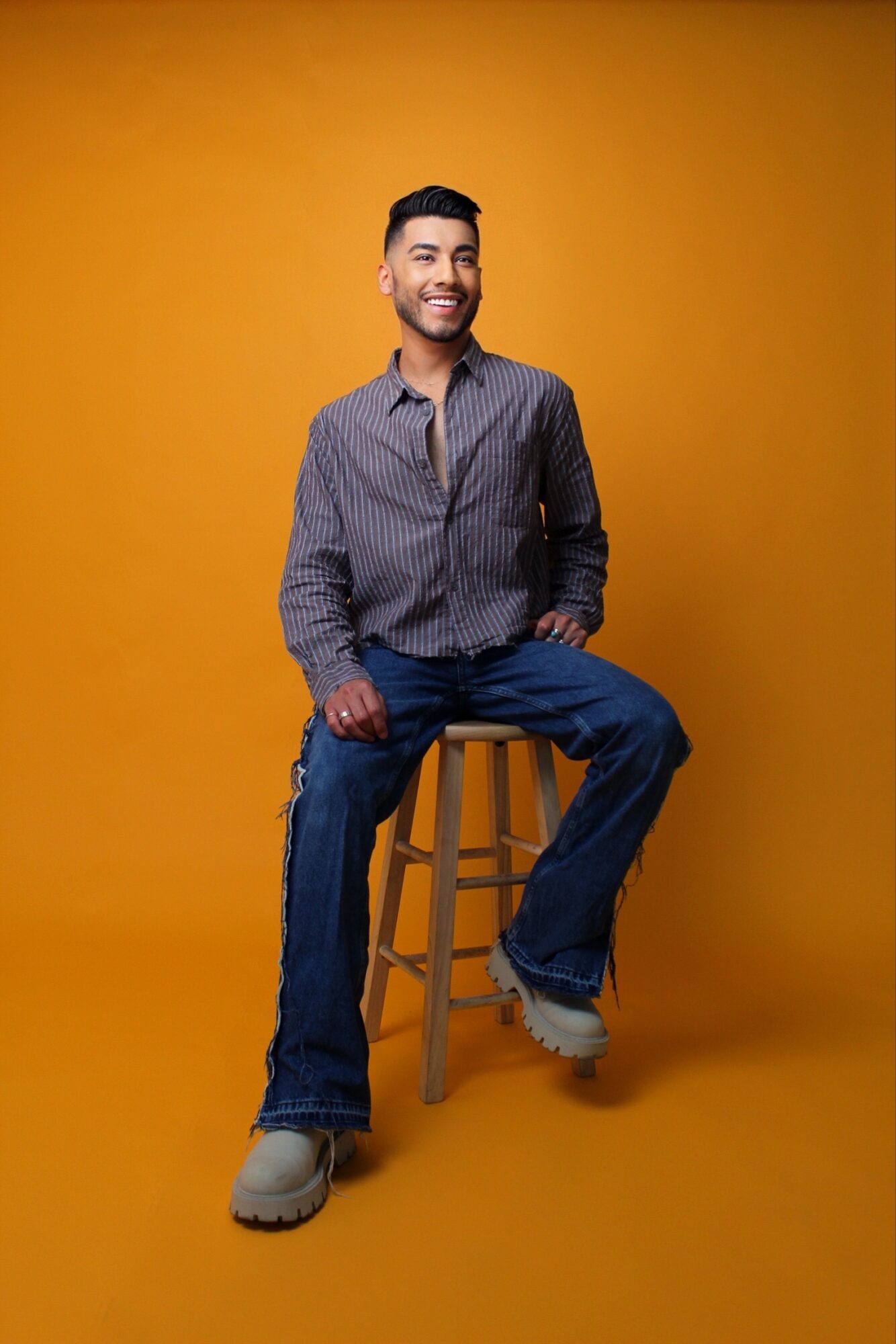 Man sitting on a stool, smiling, against a yellow background.
