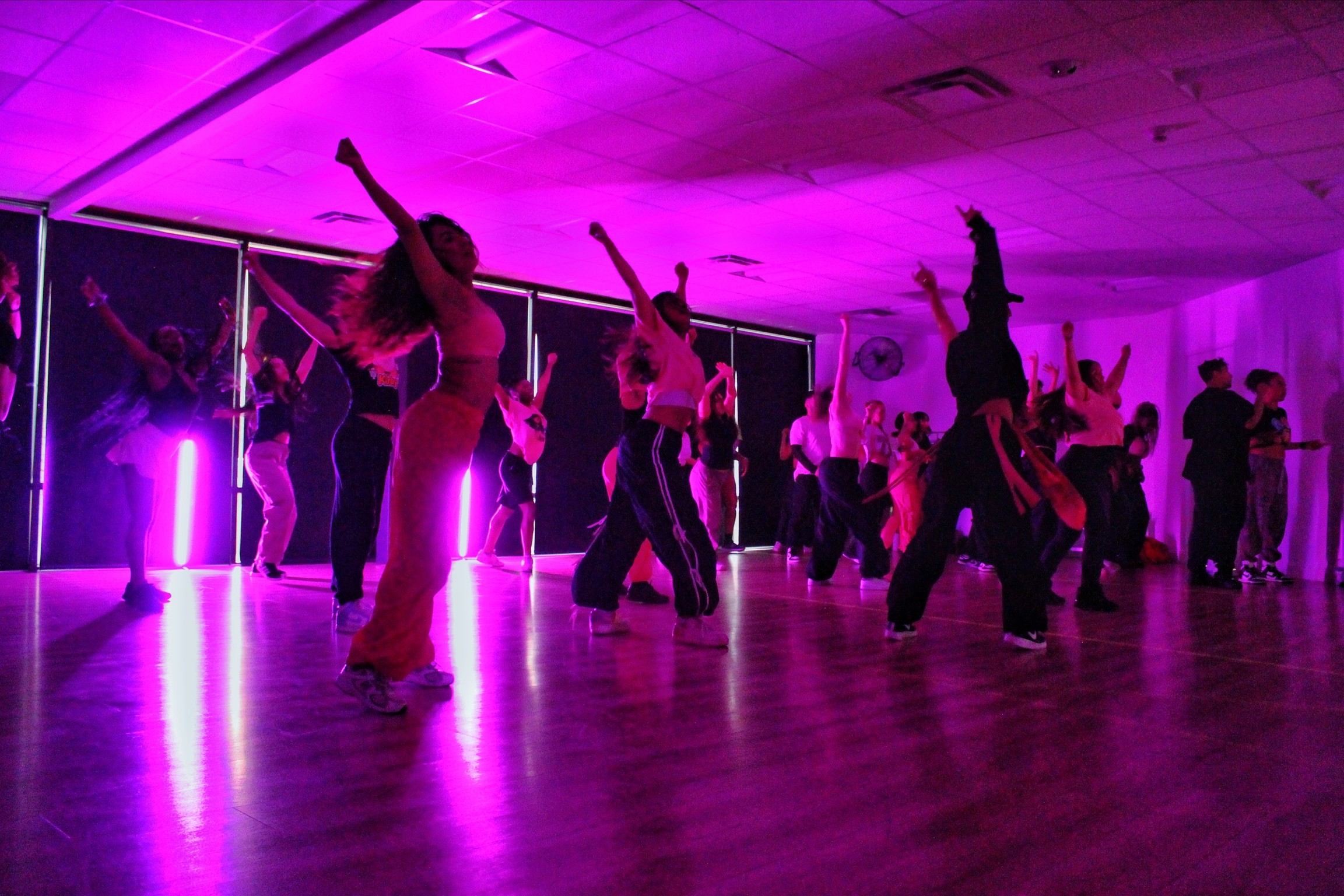 People dancing in a room with purple lighting, some with arms raised, others in various dance poses.