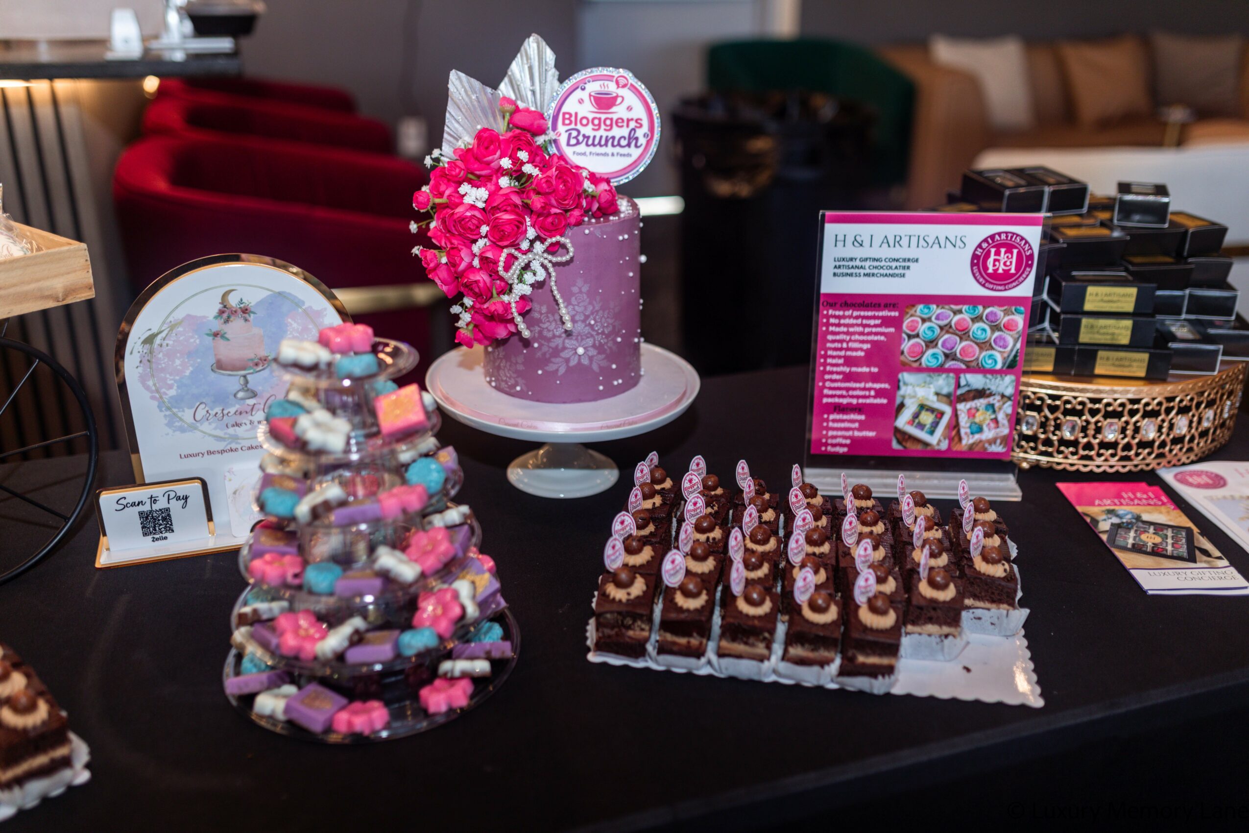 Table with pink floral cake, chocolate desserts, and decorative items in a cozy room.