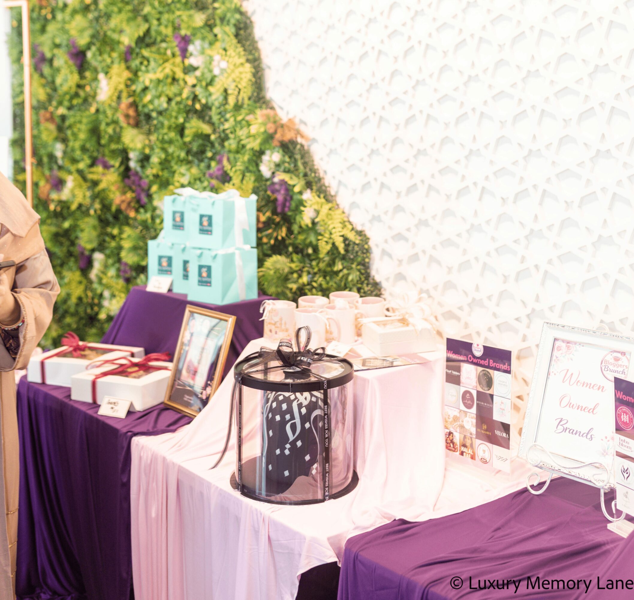Table with gift boxes, framed photo, and a black and white bag, against a floral and white textured wall.