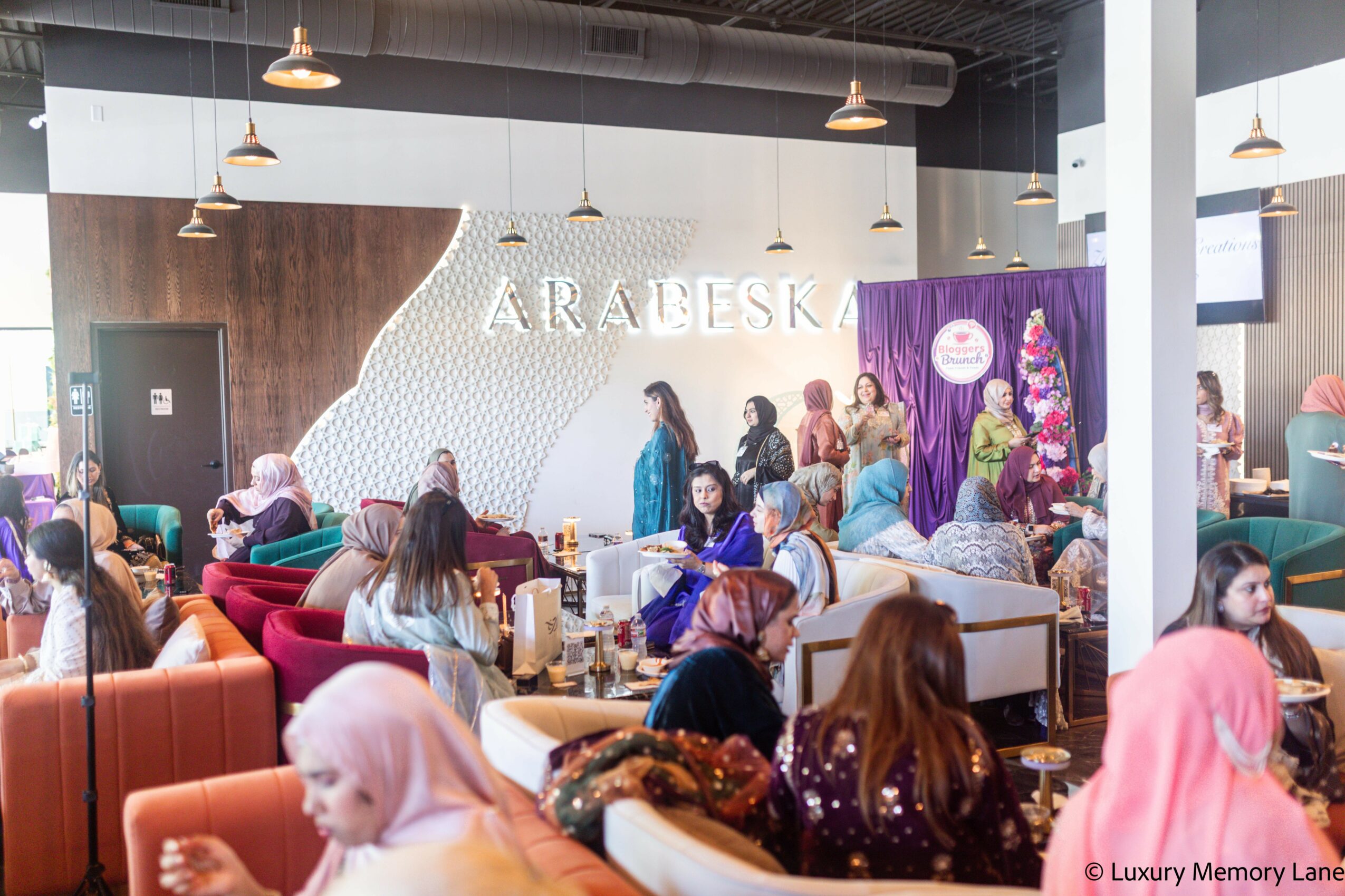 People gather in a modern indoor space with seating, a purple curtain, and a sign reading 'ARABESK' on the wall.