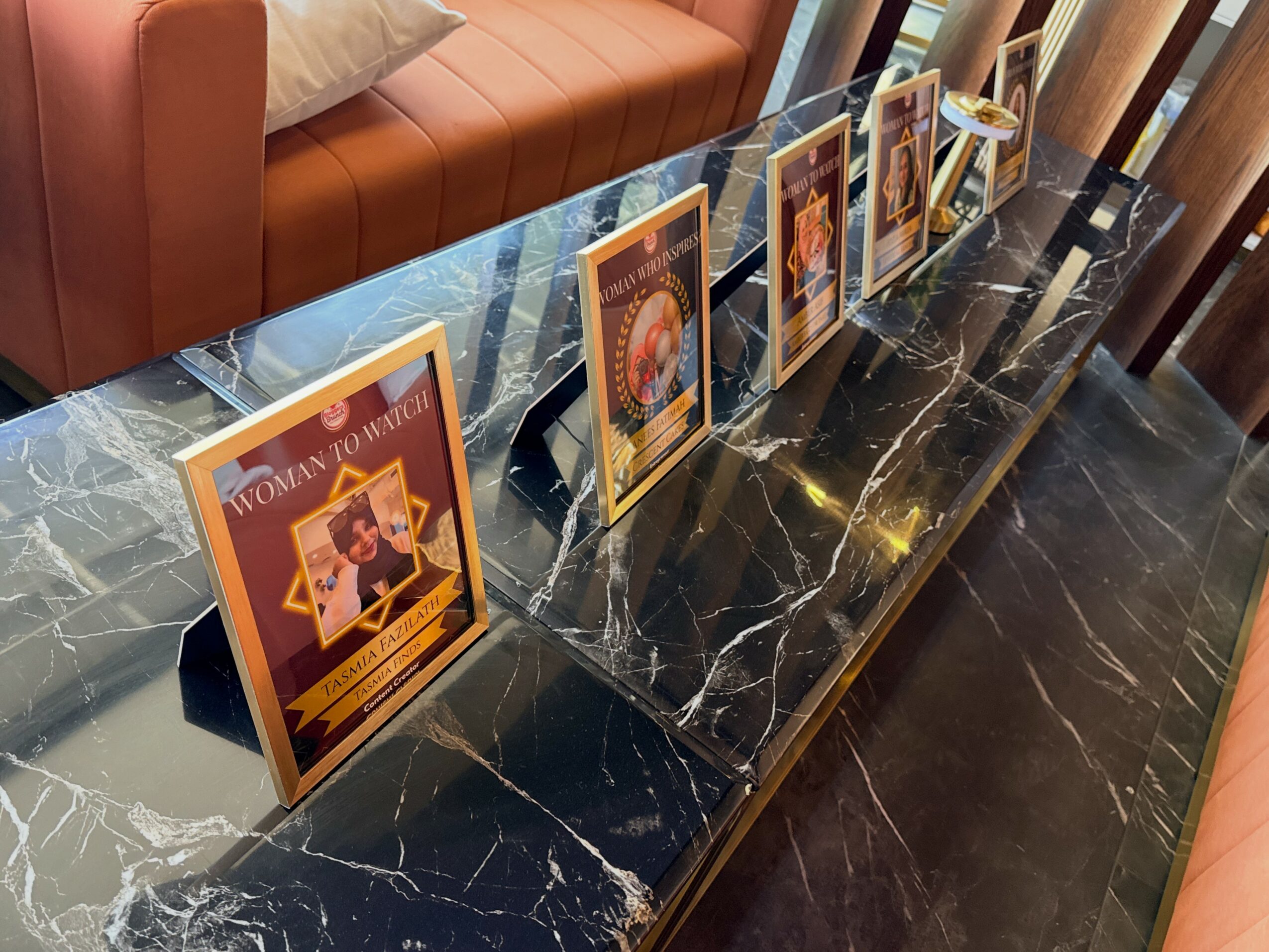 Five framed posters are displayed on a black marble table with white veins, in a room with a sofa and wooden furniture.