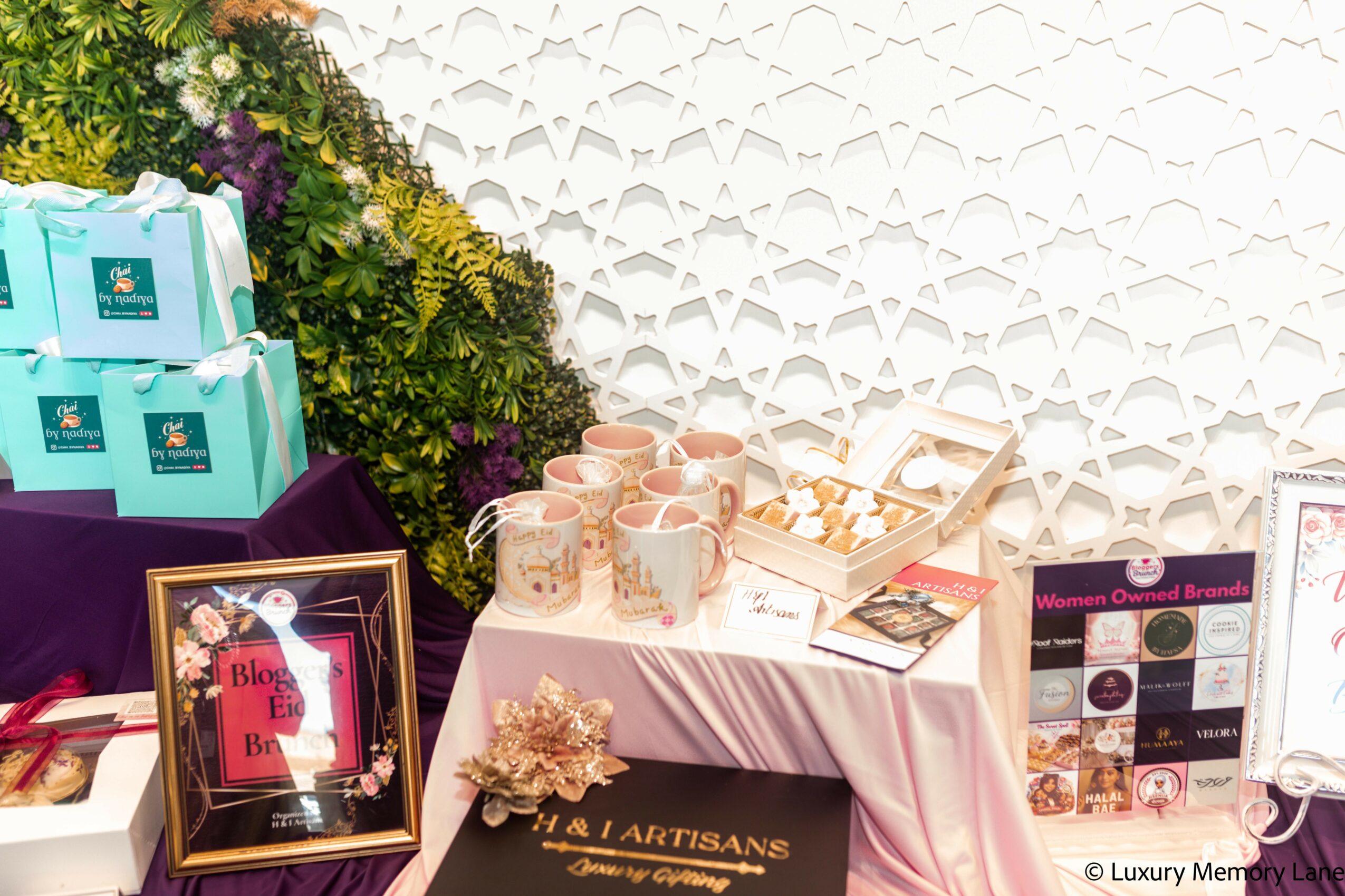 Table with cups, brochures, and decorative items, decorated with flowers and framed pictures, against a white patterned wall.