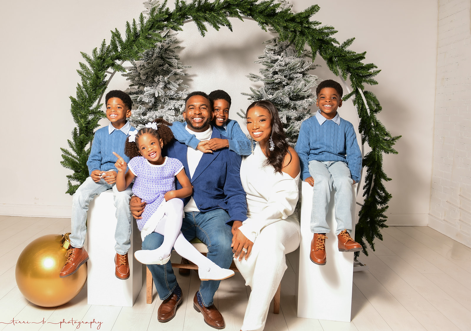 Family of six sitting and standing under a green arch with Christmas decorations, smiling indoors.