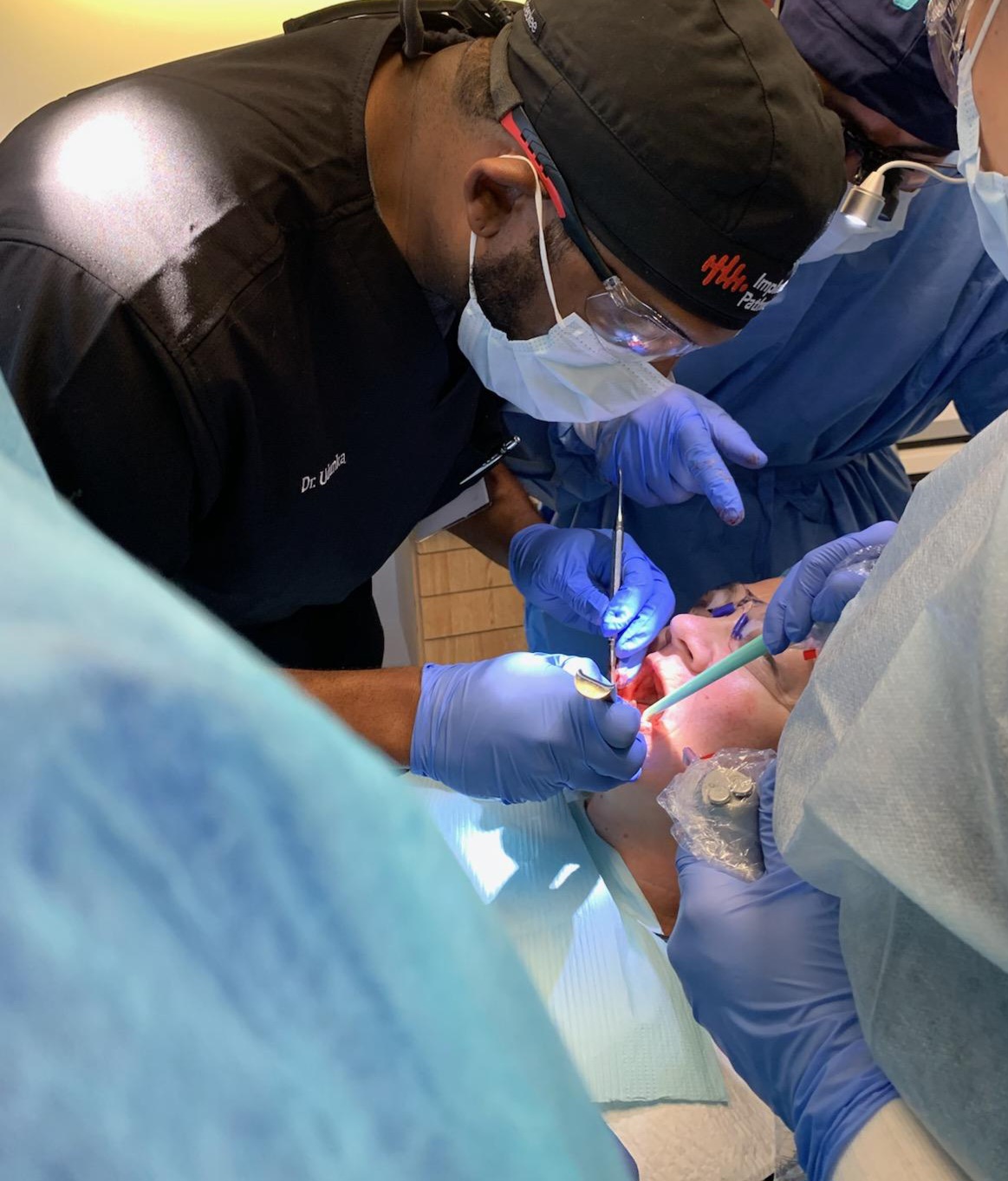 Medical professionals perform a dental procedure on a patient, wearing masks, gloves, and protective gear.