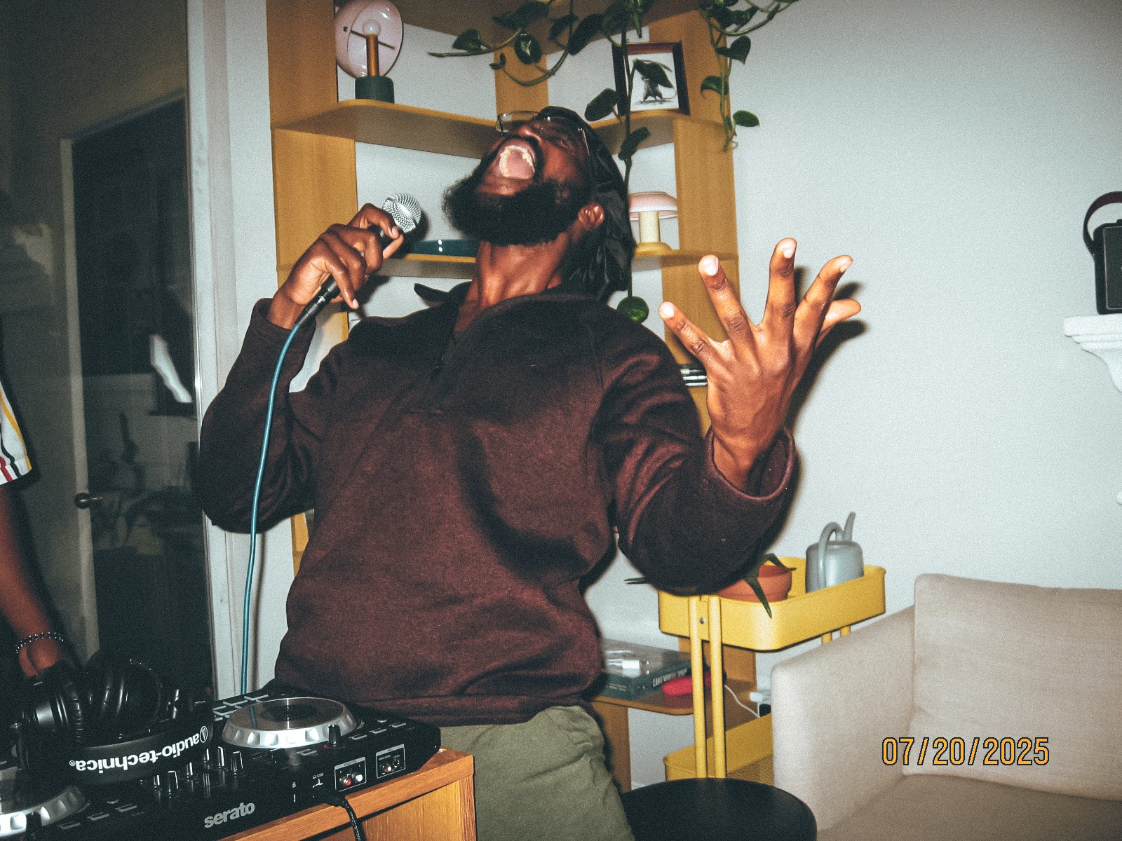 Person singing passionately with microphone in hand, eyes closed, in a room with shelves and a beige chair.