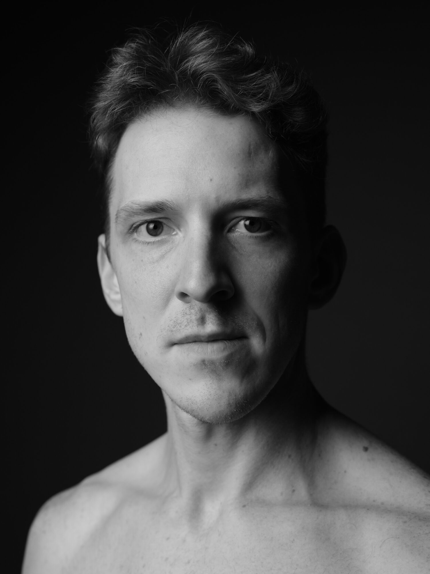 Black and white portrait of a young man with short, wavy hair, looking directly at the camera with a neutral expression.