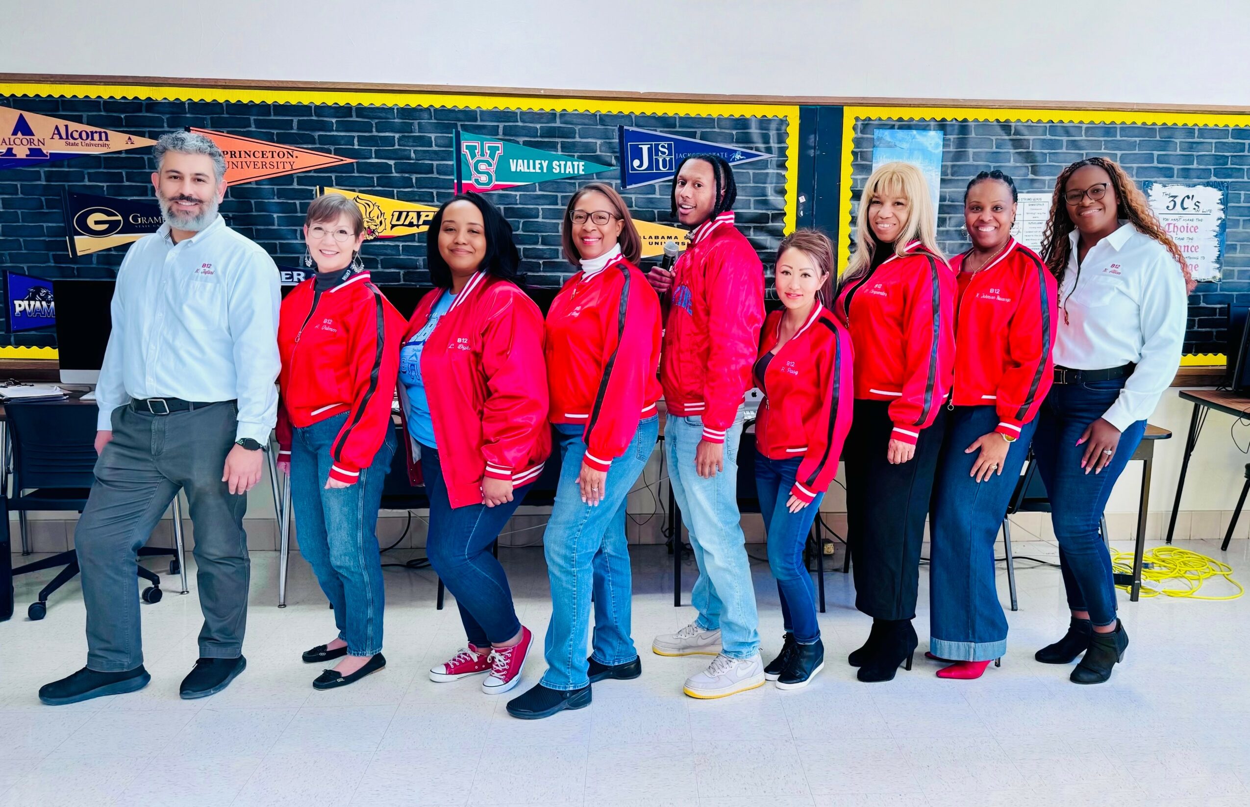 Group of nine people standing indoors in front of a colorful background, smiling and posing for the photo.