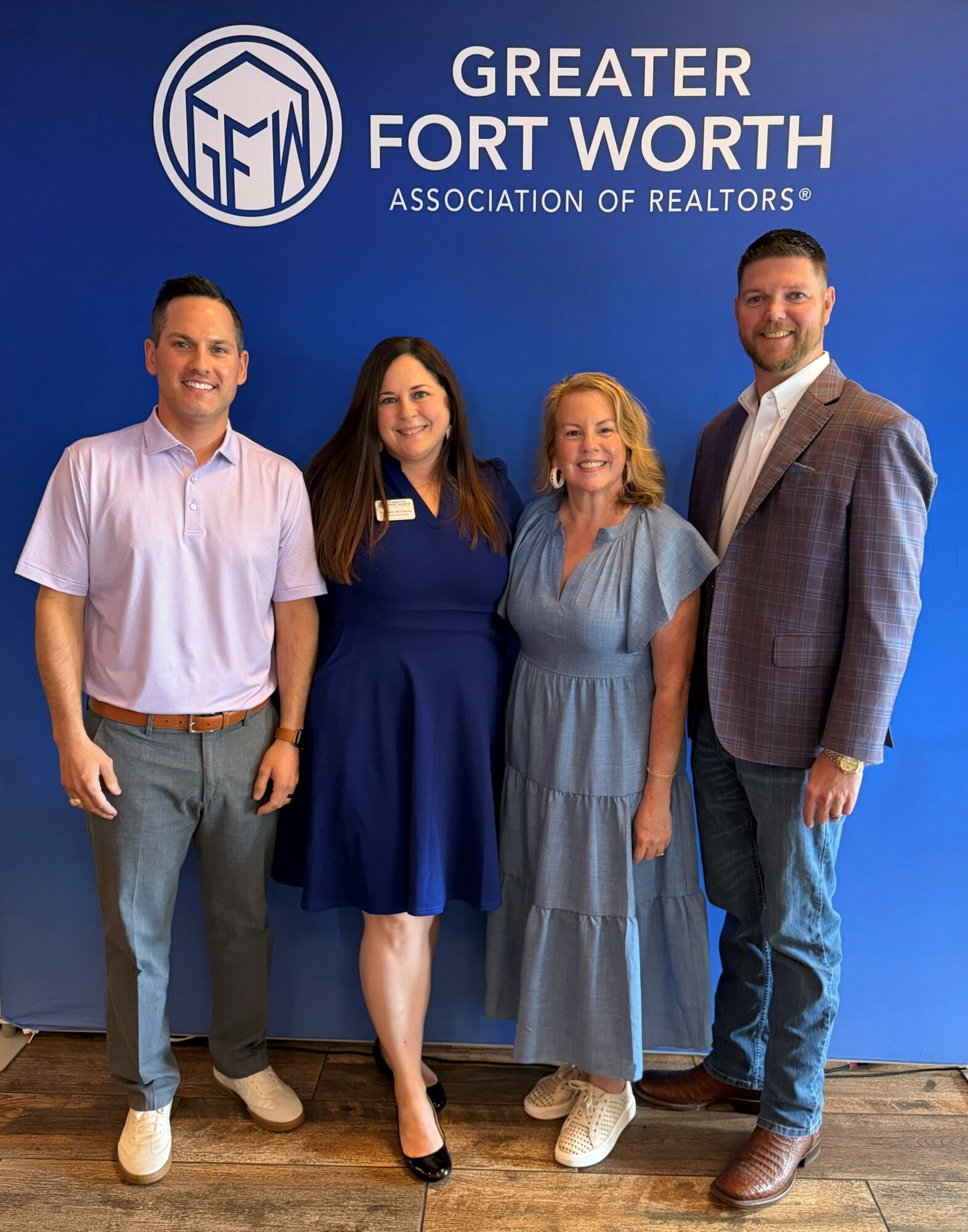 Four people standing in front of a blue wall with the Greater Fort Worth Association of Realtors logo, smiling.