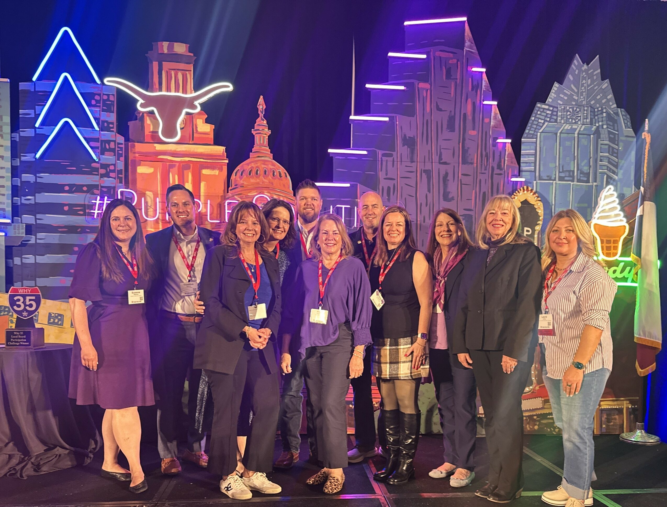 Group of people standing together in front of colorful neon cityscape backdrop, smiling for photo.