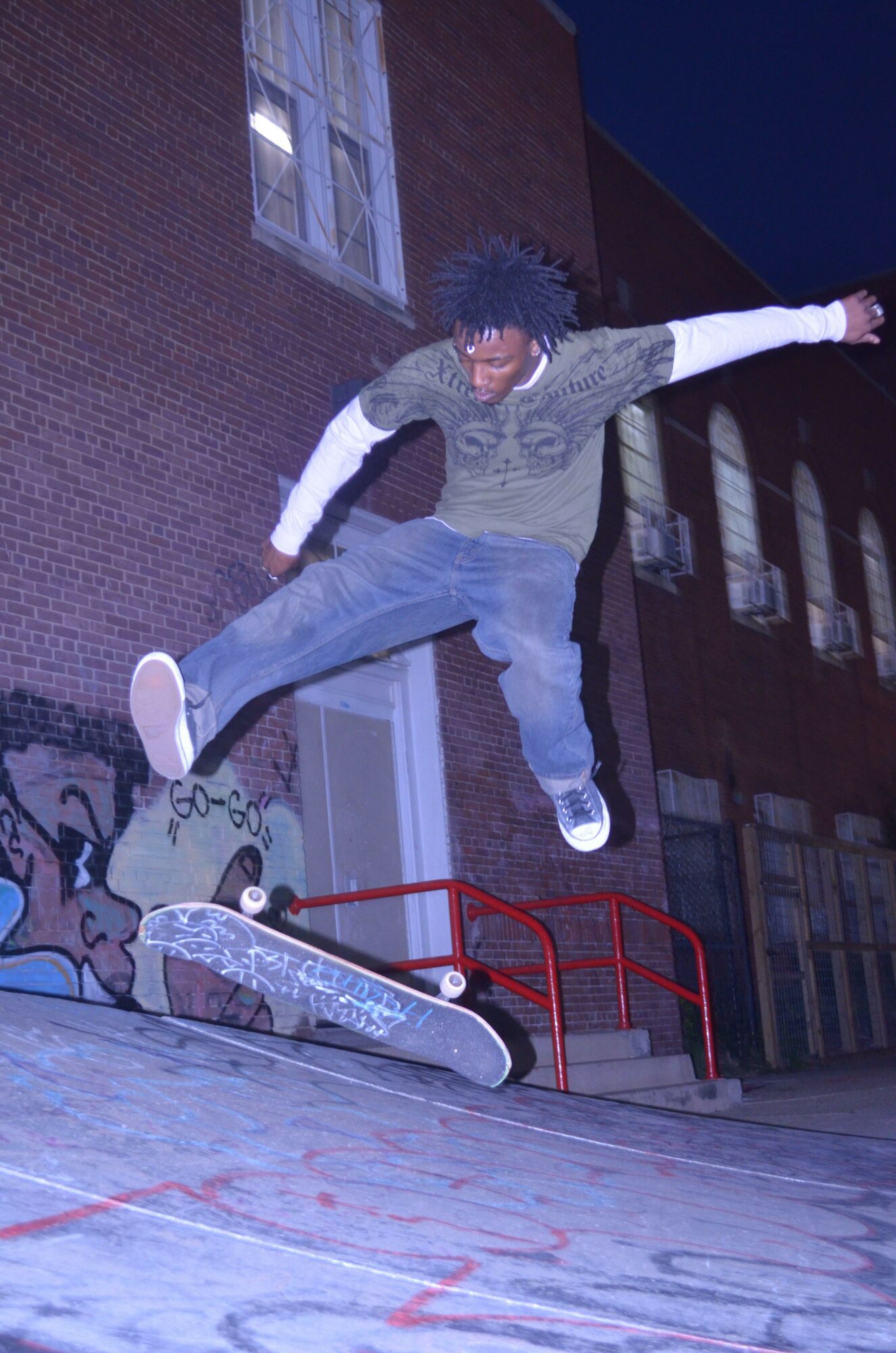 Skateboarder mid-air performing a trick on a skate ramp at night, with a brick building in the background.