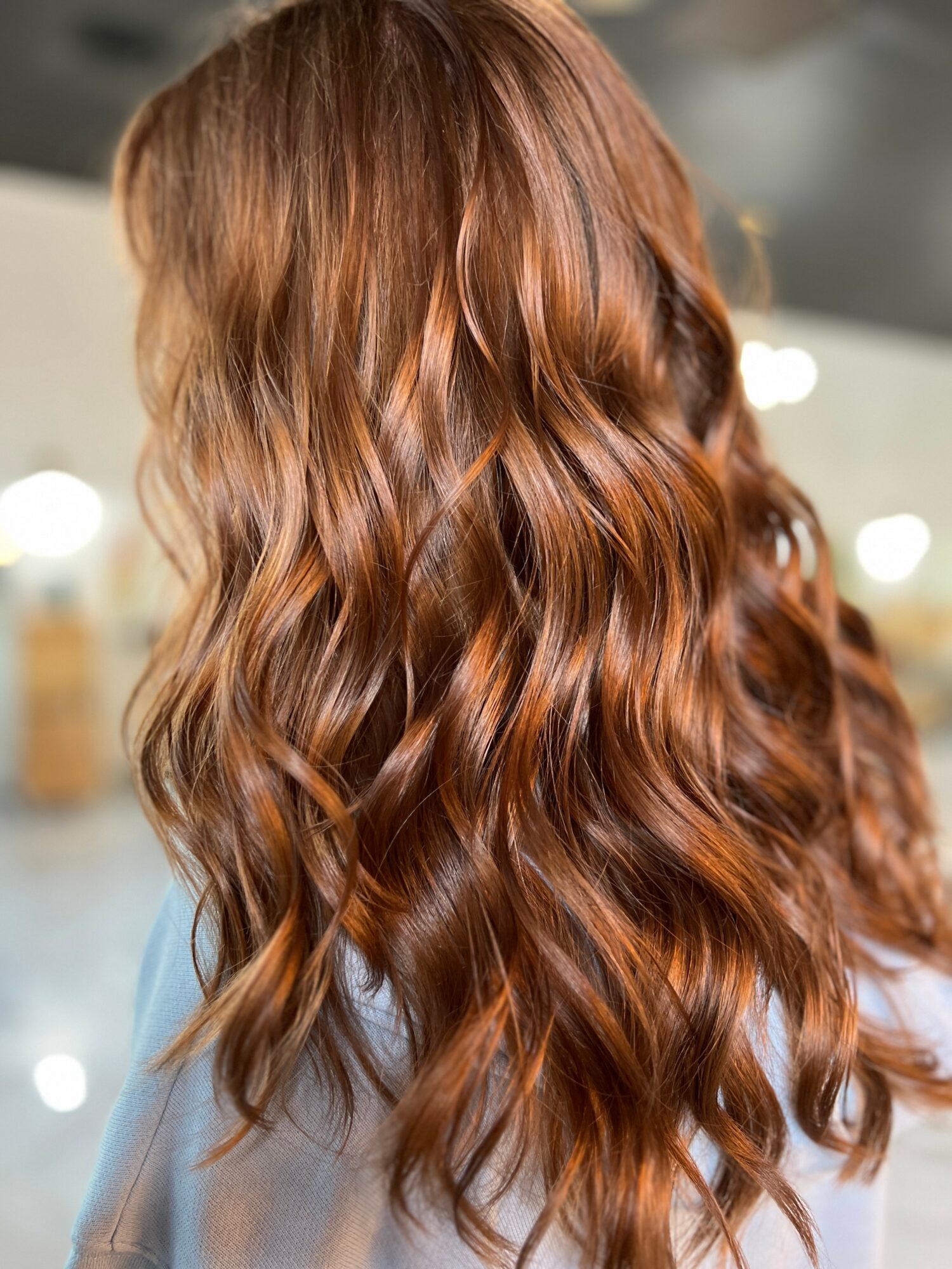 Back of a person with long, wavy, reddish-brown hair in an indoor setting.