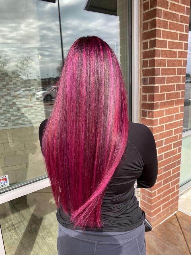 Person with long, straight, vibrant pink hair standing outside near a brick wall and window.