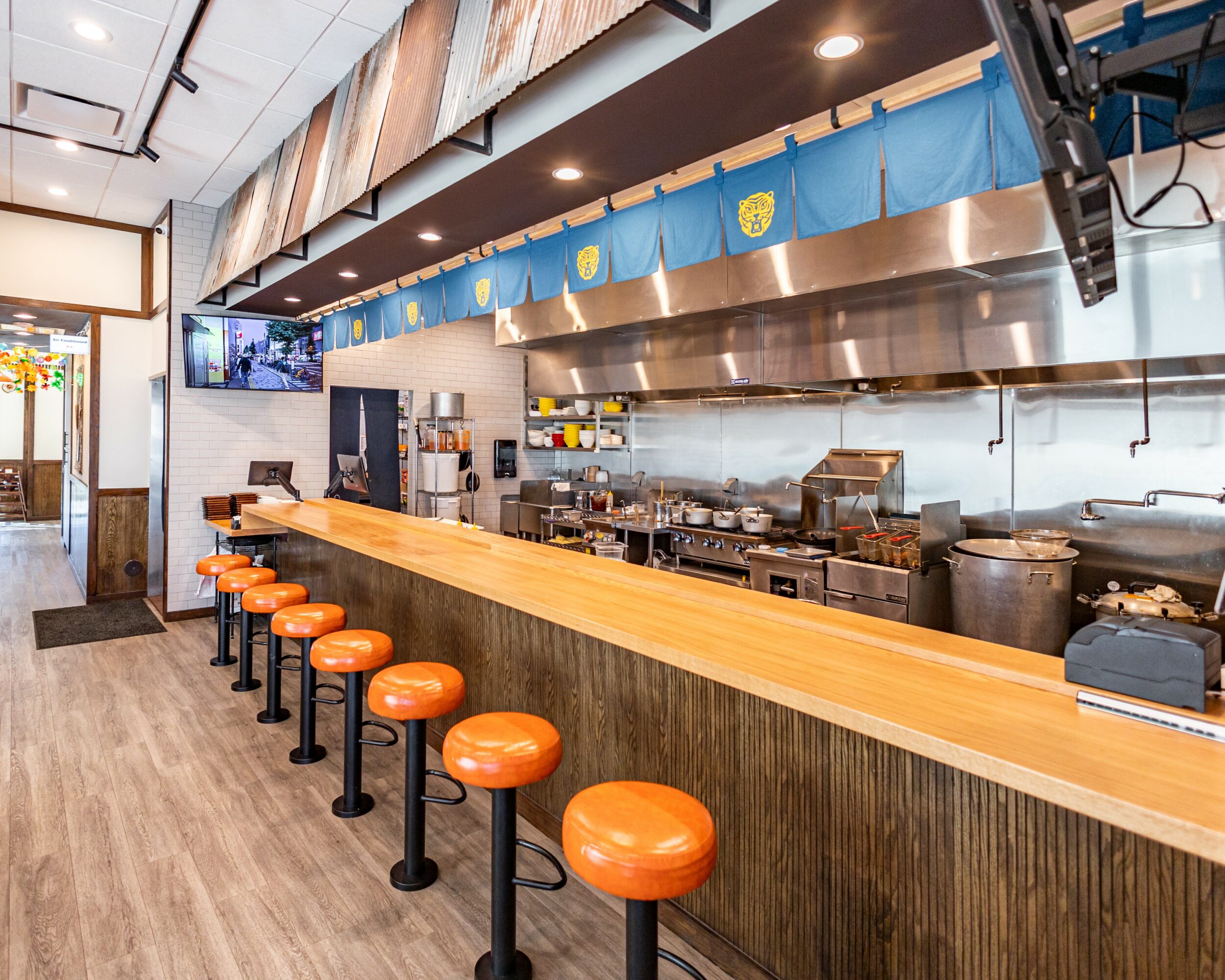 Long wooden counter with orange stools in front, open kitchen with stainless steel appliances and blue decor above.