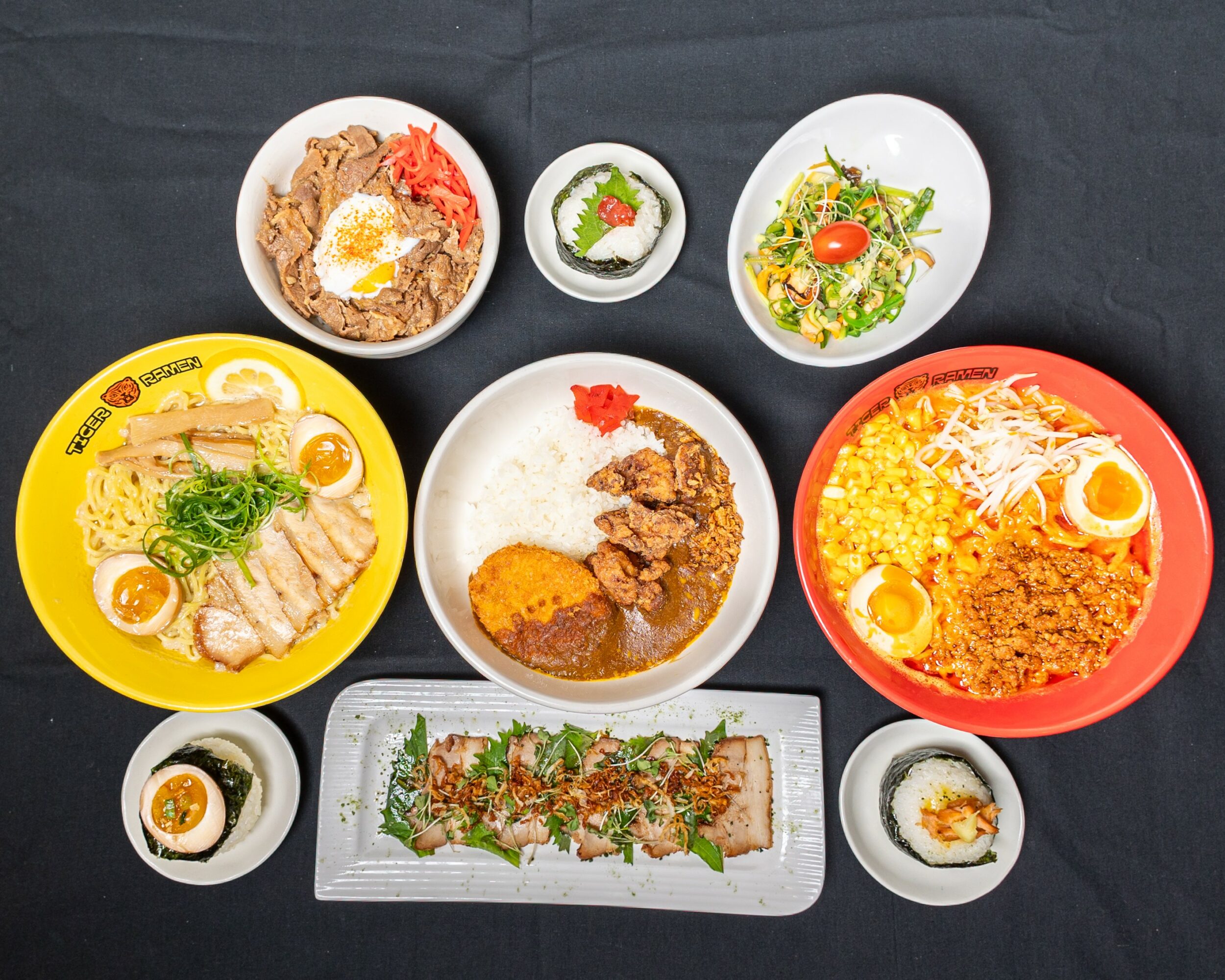 Assorted Japanese dishes including rice bowls, curry, salad, sashimi, and side dishes on a black surface.
