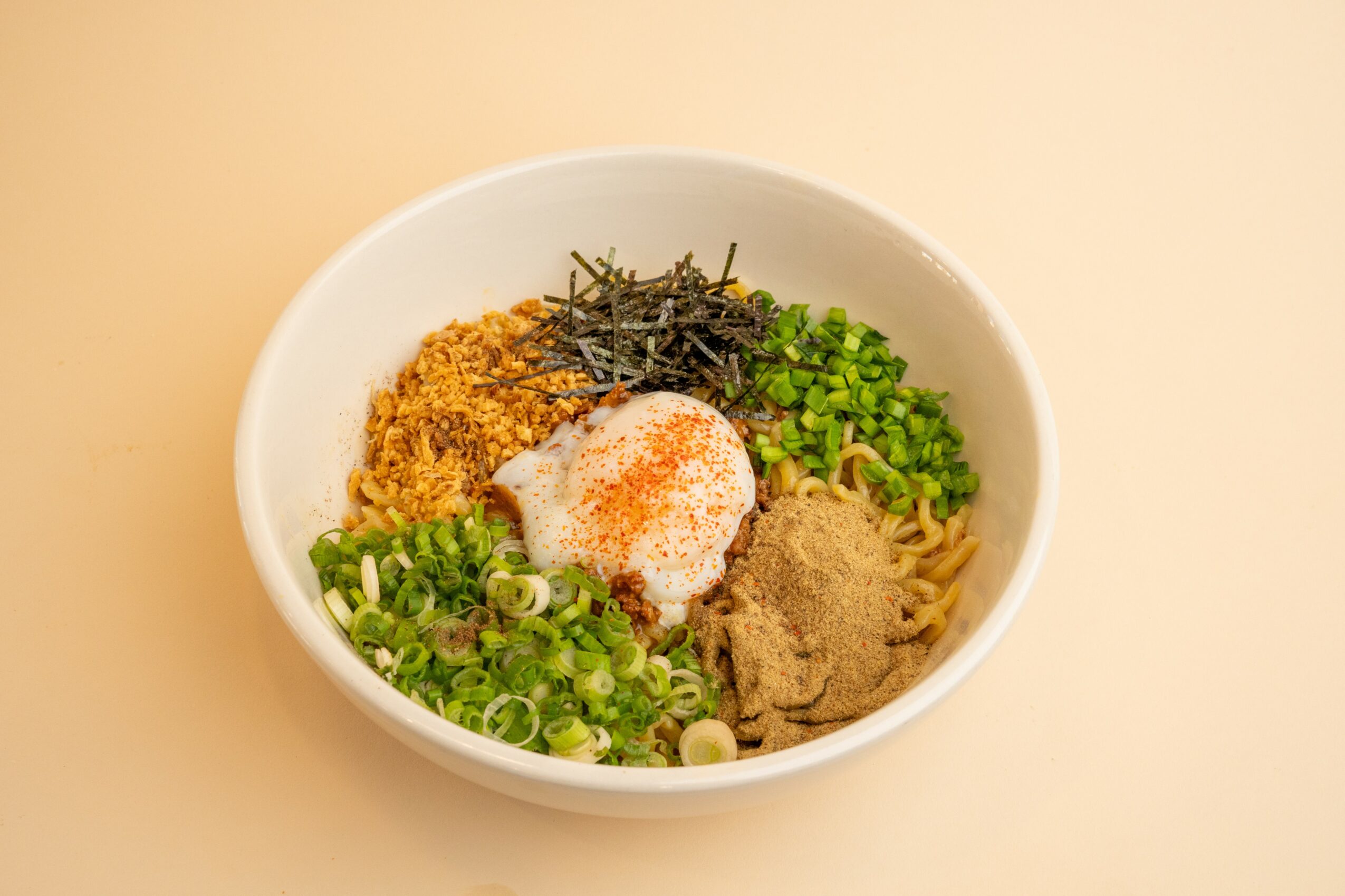 Bowl with noodles, green onions, seaweed, ground meat, and seasoning on top, arranged in sections.