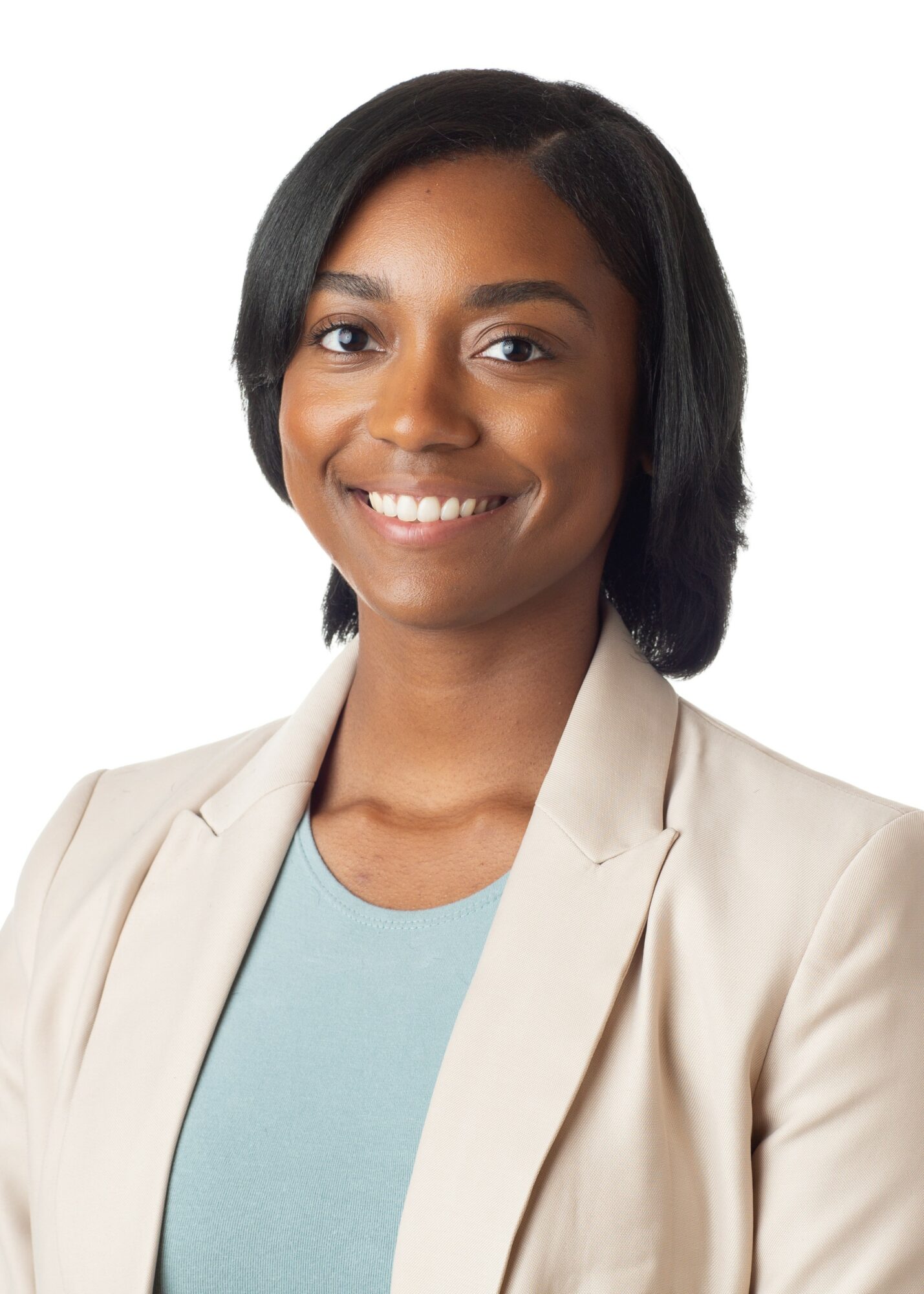 Smiling woman with shoulder-length black hair wearing a beige blazer and light blue top.