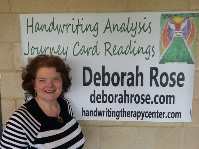 Woman with curly hair smiling in front of a sign about handwriting analysis and card reading.
