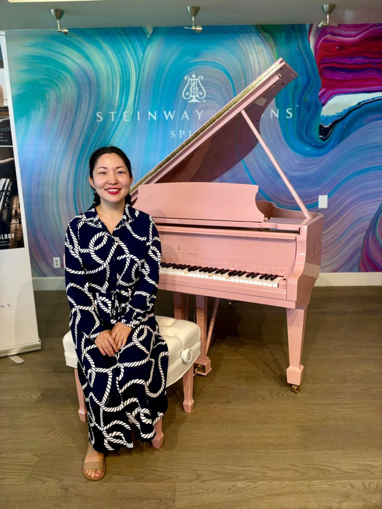 Woman in patterned dress standing next to pink grand piano in art gallery setting.