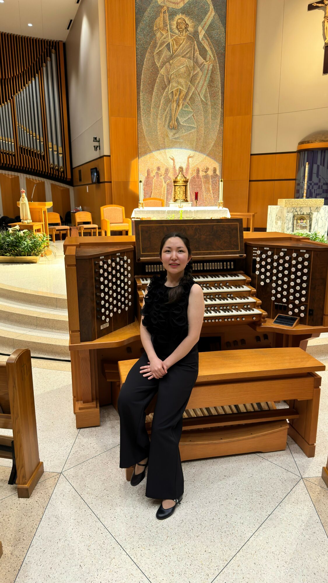 Woman sitting in front of an ornate pipe organ in a church or cathedral interior.
