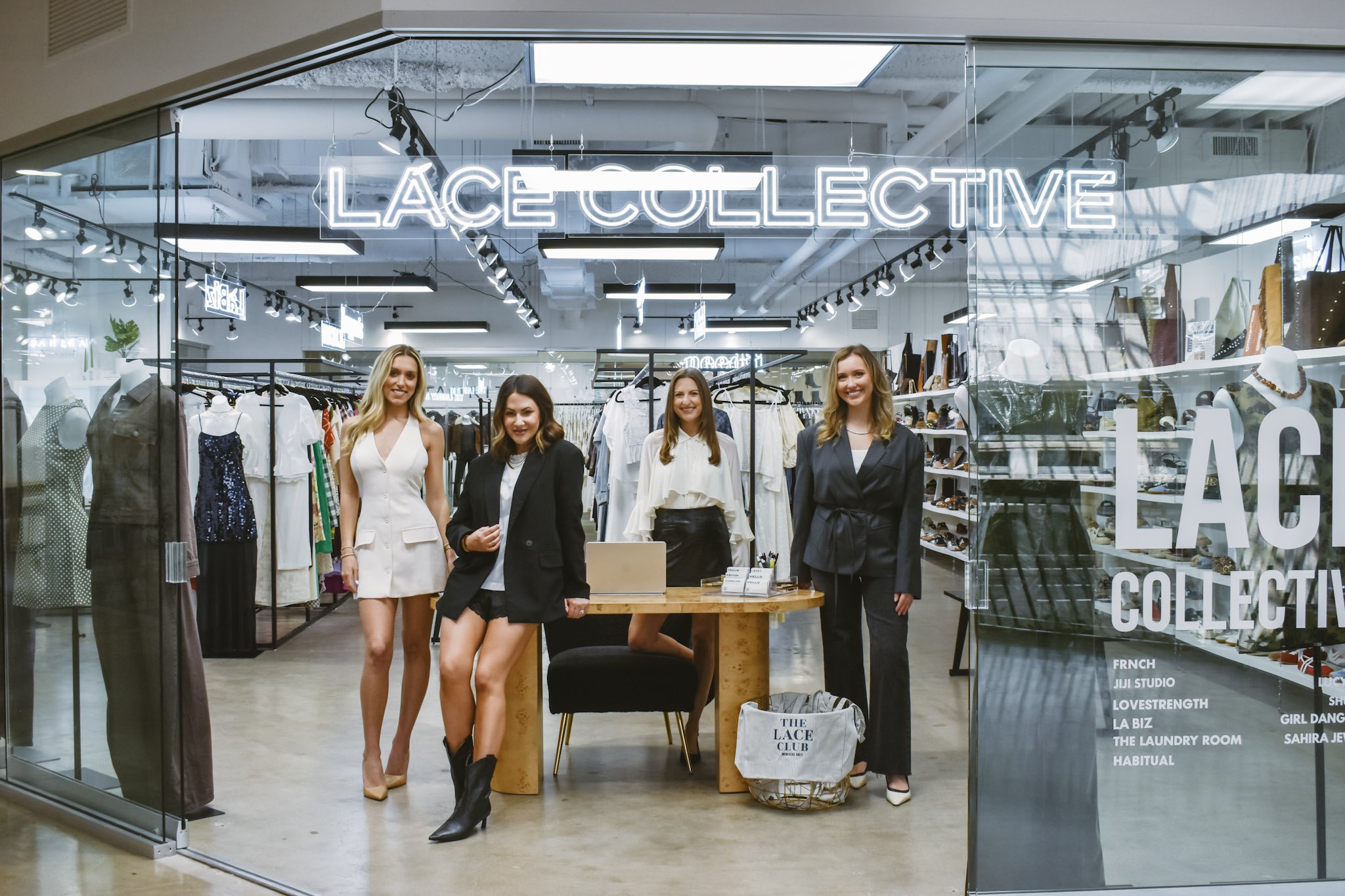 Four women stand inside a clothing store named LACE COLLECTIVE, with racks of clothes visible behind them.