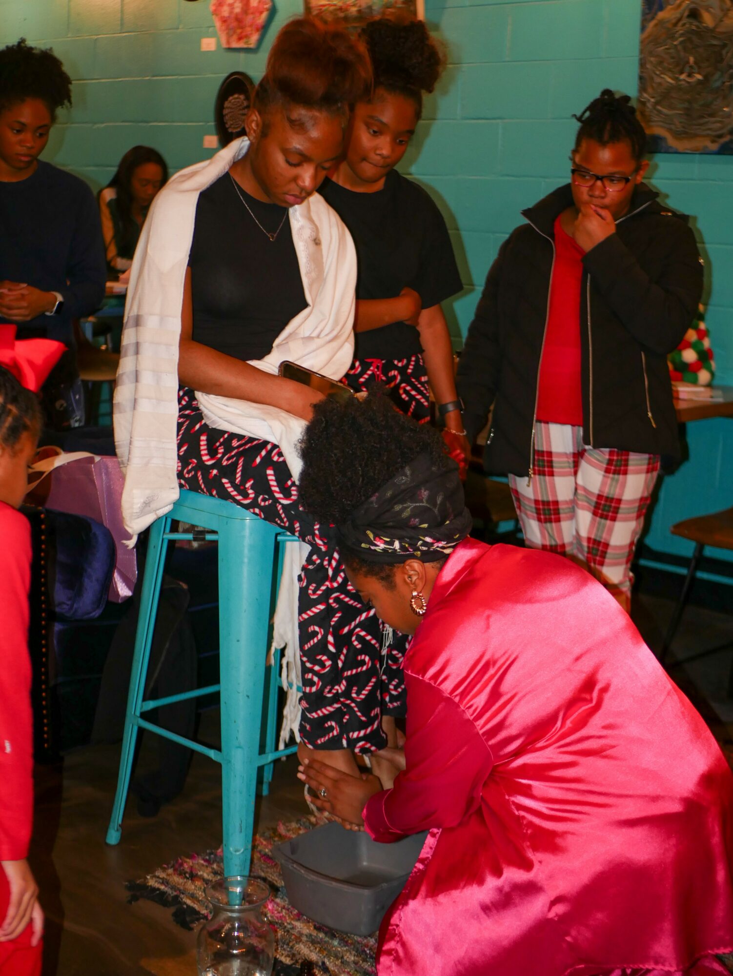 Group of young women gathered around a person in a pink dress, with one sitting on a stool and others standing nearby.