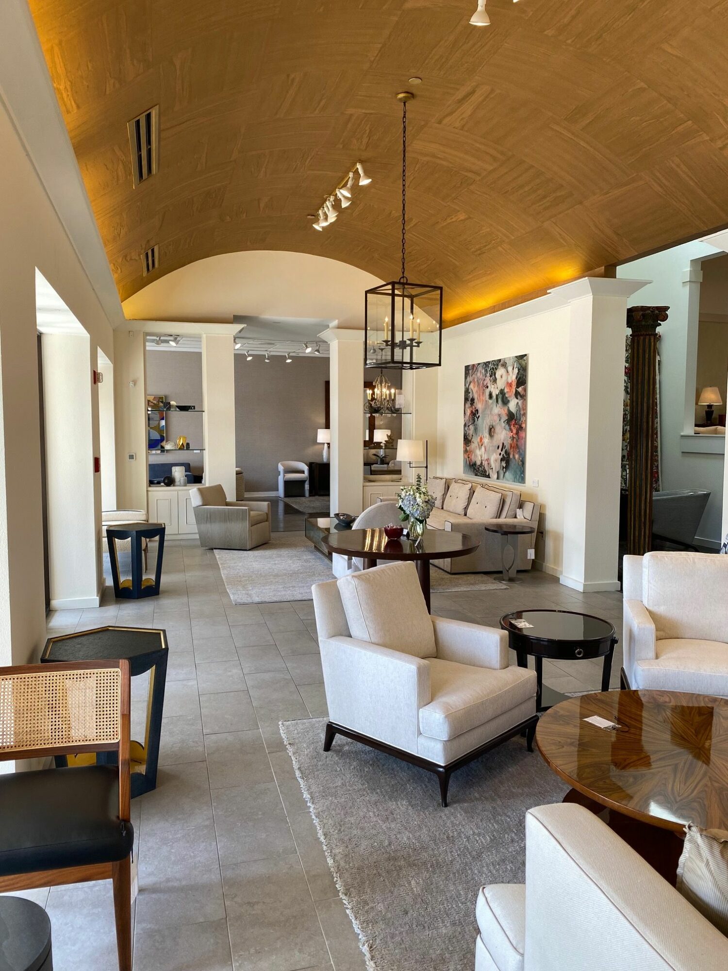 Elegant lounge with white armchairs, a sofa, and a wooden table, decorated with artwork and a hanging light fixture.