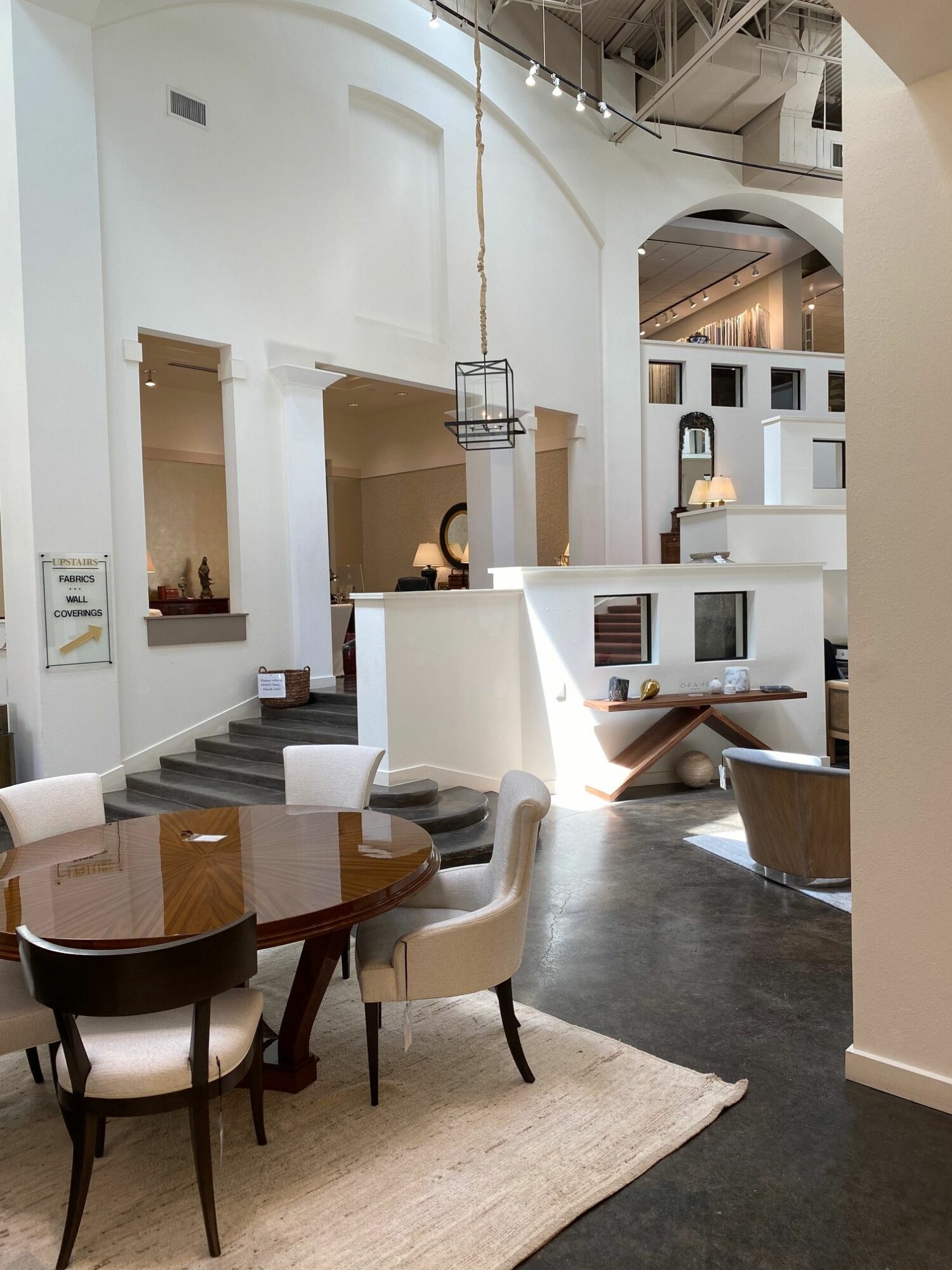 Dining area with round table, six chairs, and a beige rug in a bright, modern space with white walls and high ceilings.