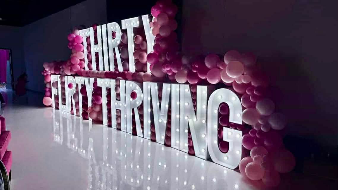 Large illuminated letters spell 'THIRST QUENCHING' with pink balloons around them.