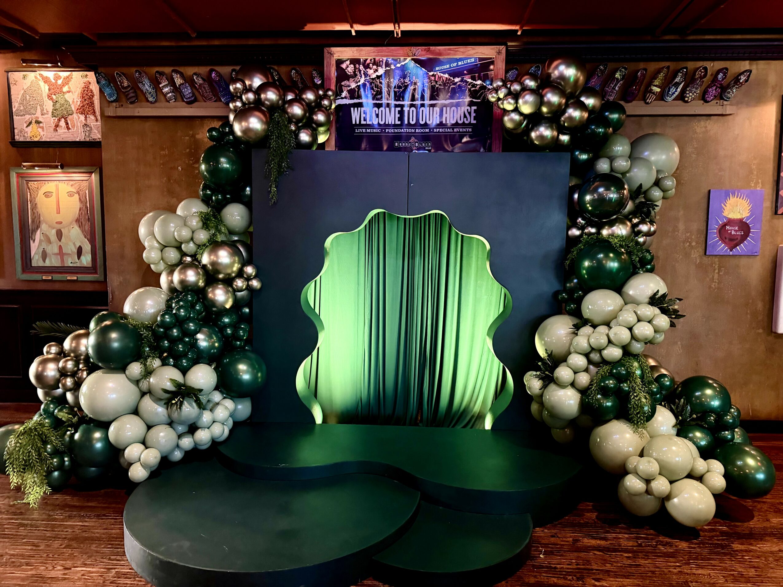 Decorative stage with green curtain and balloon arch, featuring green, white, and silver balloons, and a welcome sign.