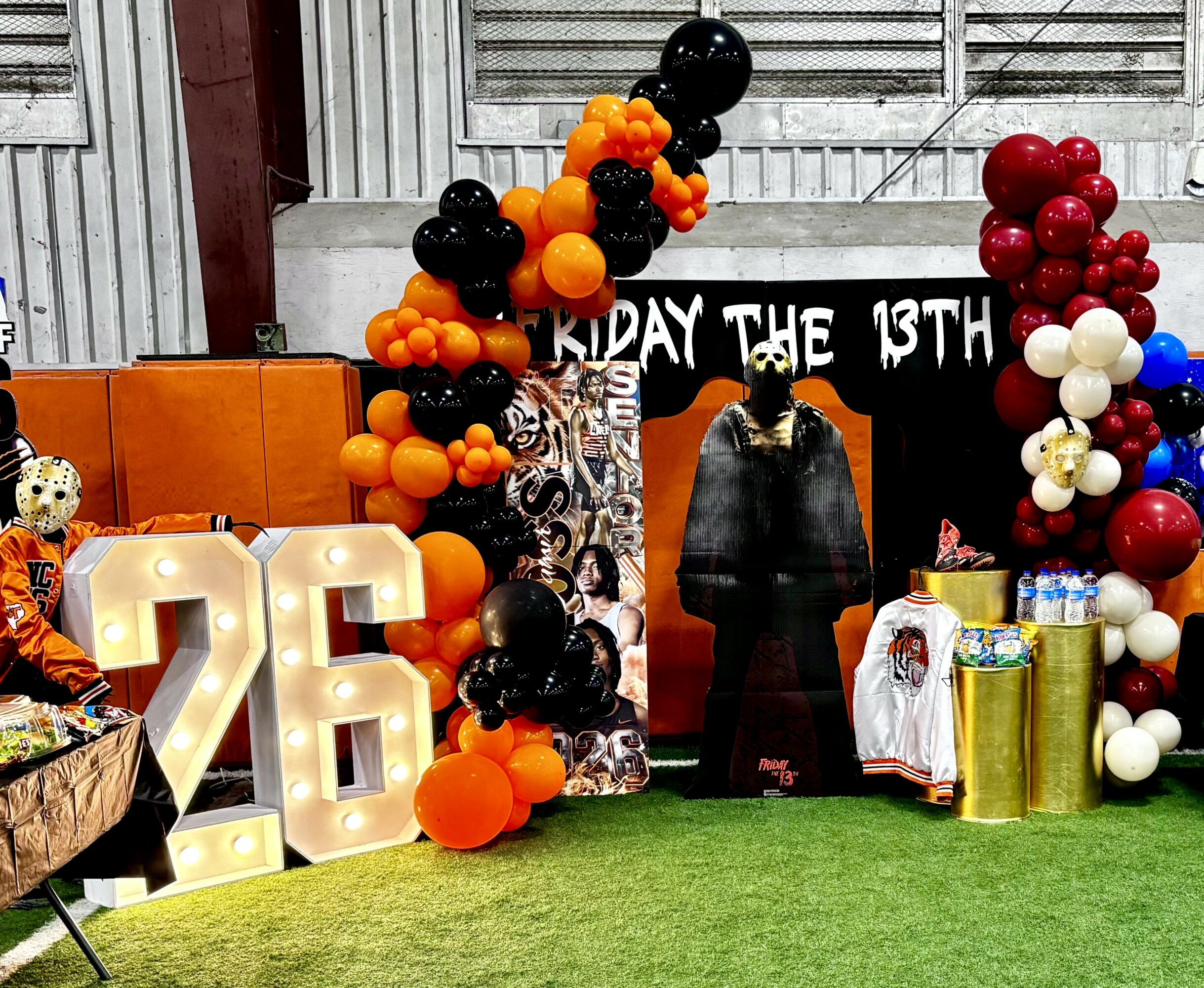 Decorations for a birthday celebration with balloons, large number 26, and a person in front of a black backdrop.