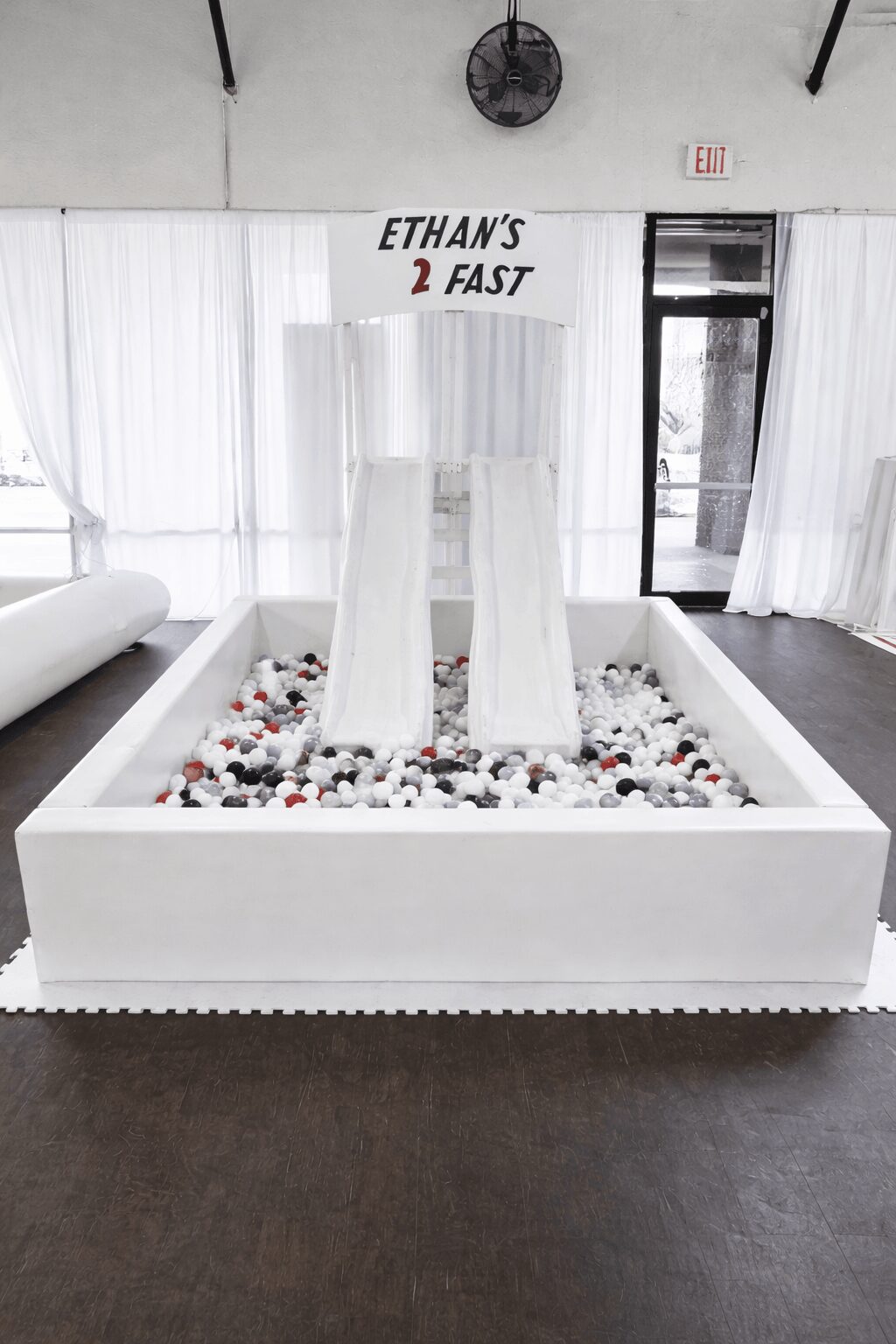 Indoor space with white fountain, rocks, and two tall white structures, curtains, and a door in the background.