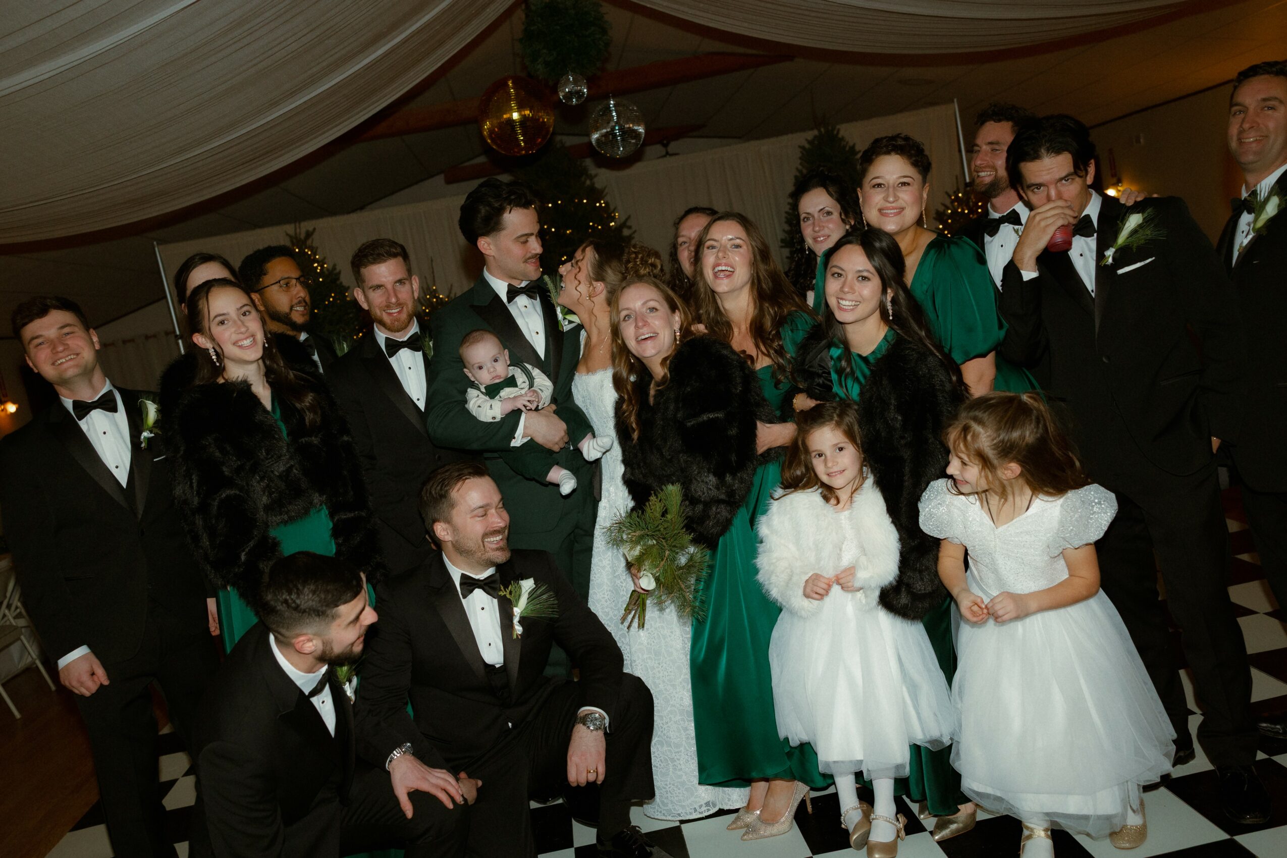 Group of people dressed in formal attire, some children in white dresses, gathered indoors for celebration.