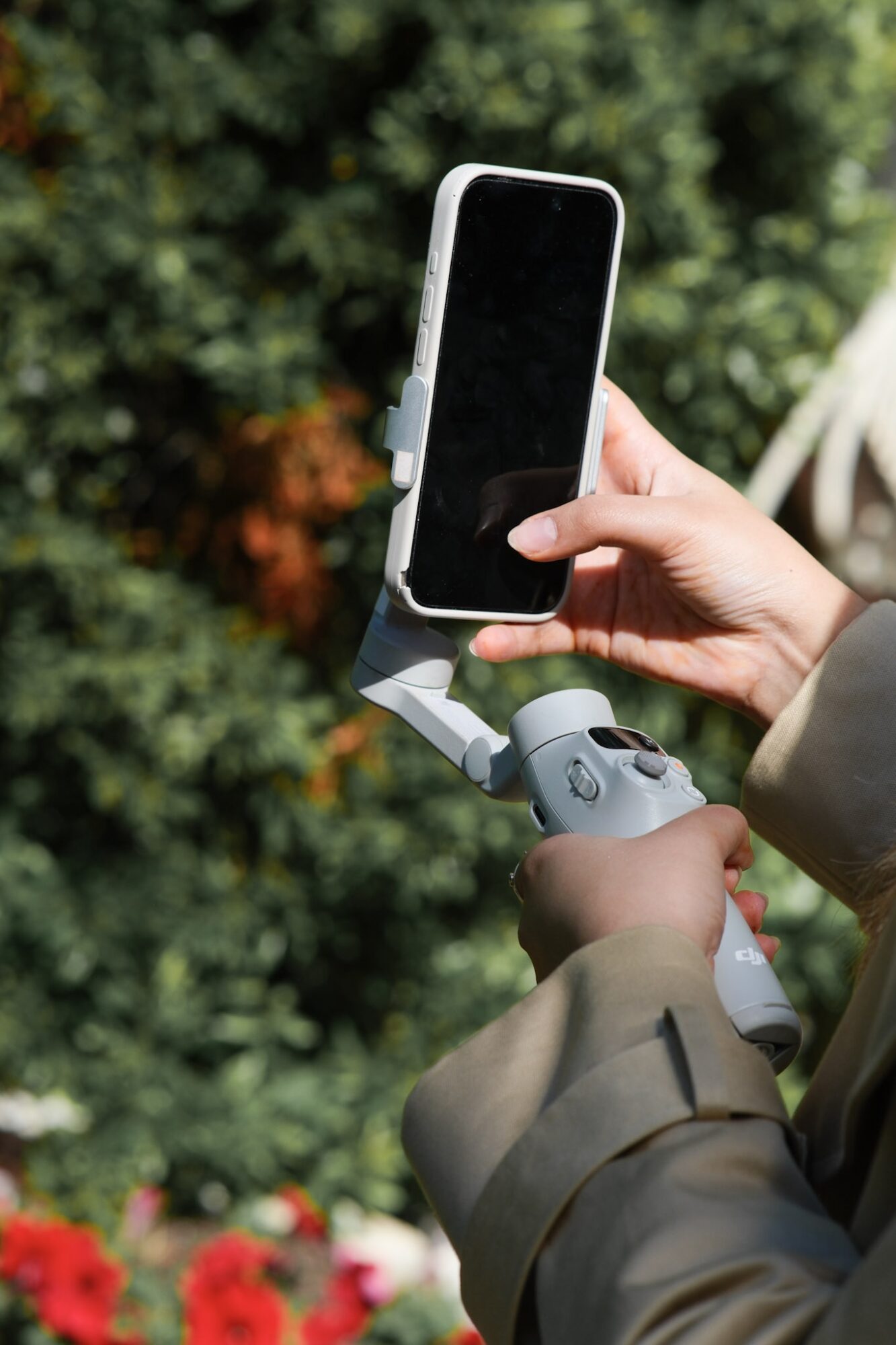 Person holding a smartphone mounted on a stabilizer outdoors with green foliage background.