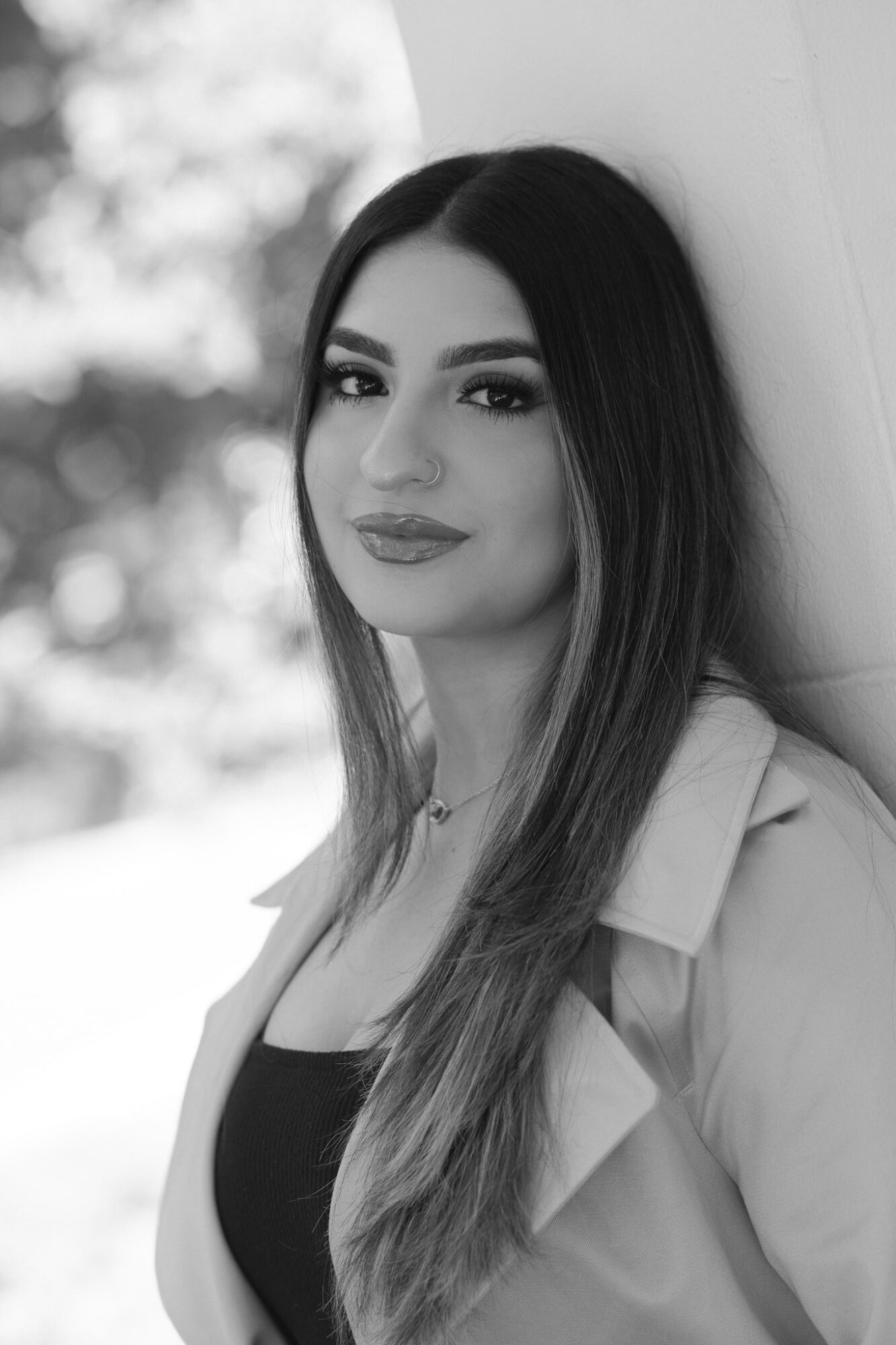 Woman with long hair, smiling, leaning against a wall outdoors, black and white photo.