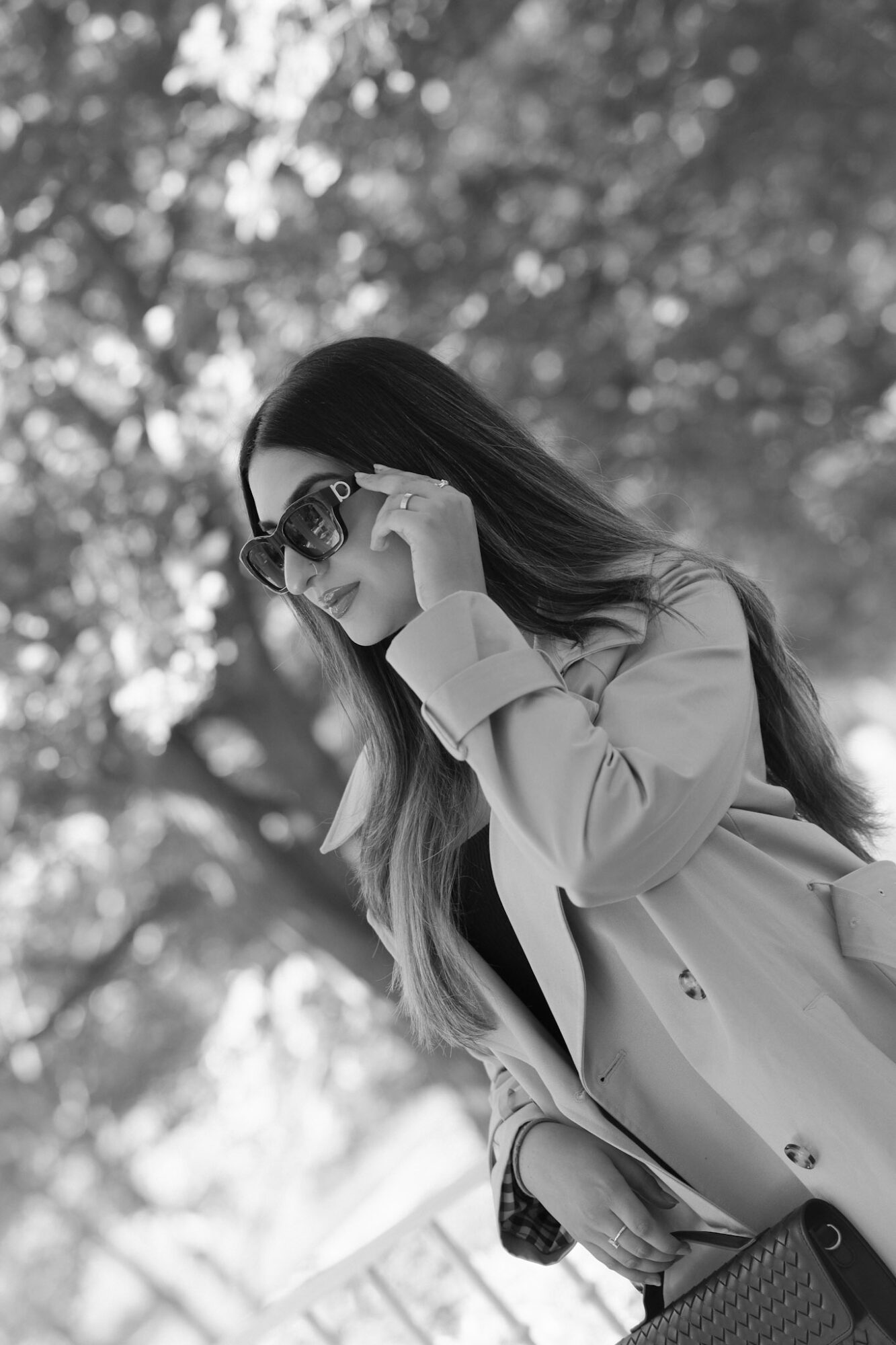 Woman with long hair wearing sunglasses and headphones, outdoors with trees in background.