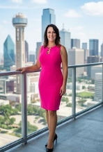 Woman in pink dress standing on balcony with city skyline in background.