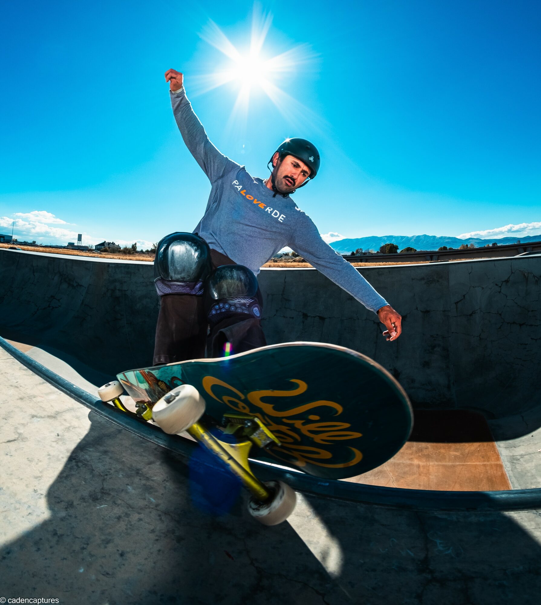 Skateboarder in a skatepark with a sunny sky, wearing a helmet and protective gear, balancing on a ramp.